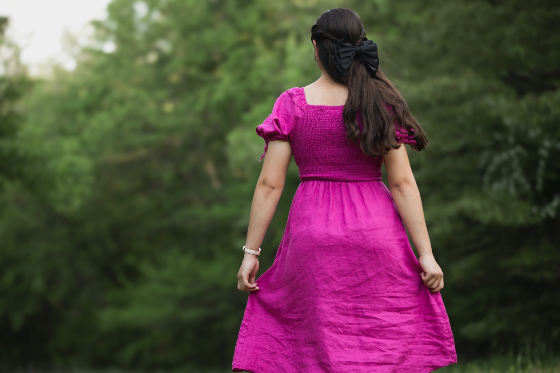 Woman in a pink modest nursing dress walking away with trees in the background