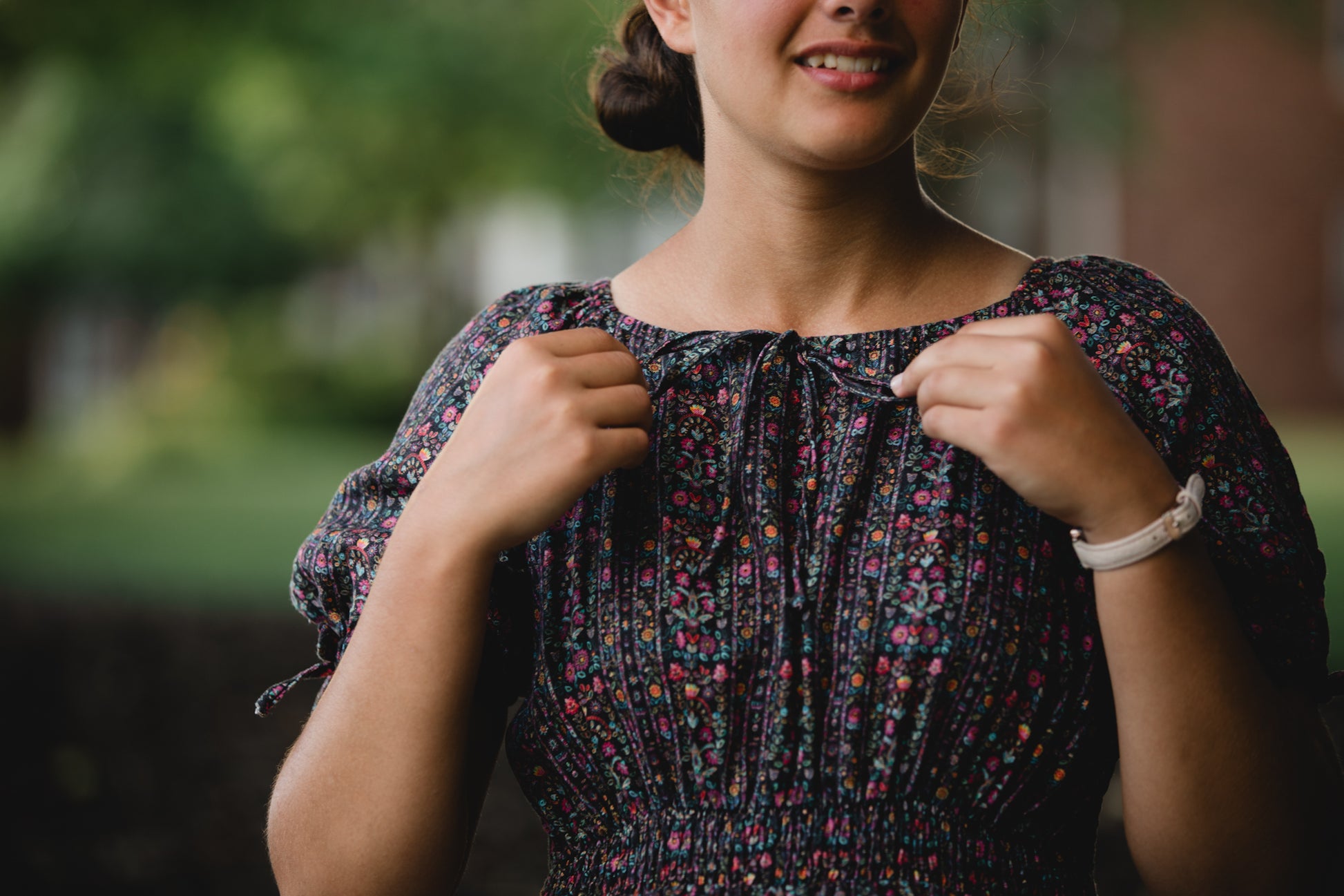 Woman adjusting her floral modest nursing dress outdoors with a blurred background
