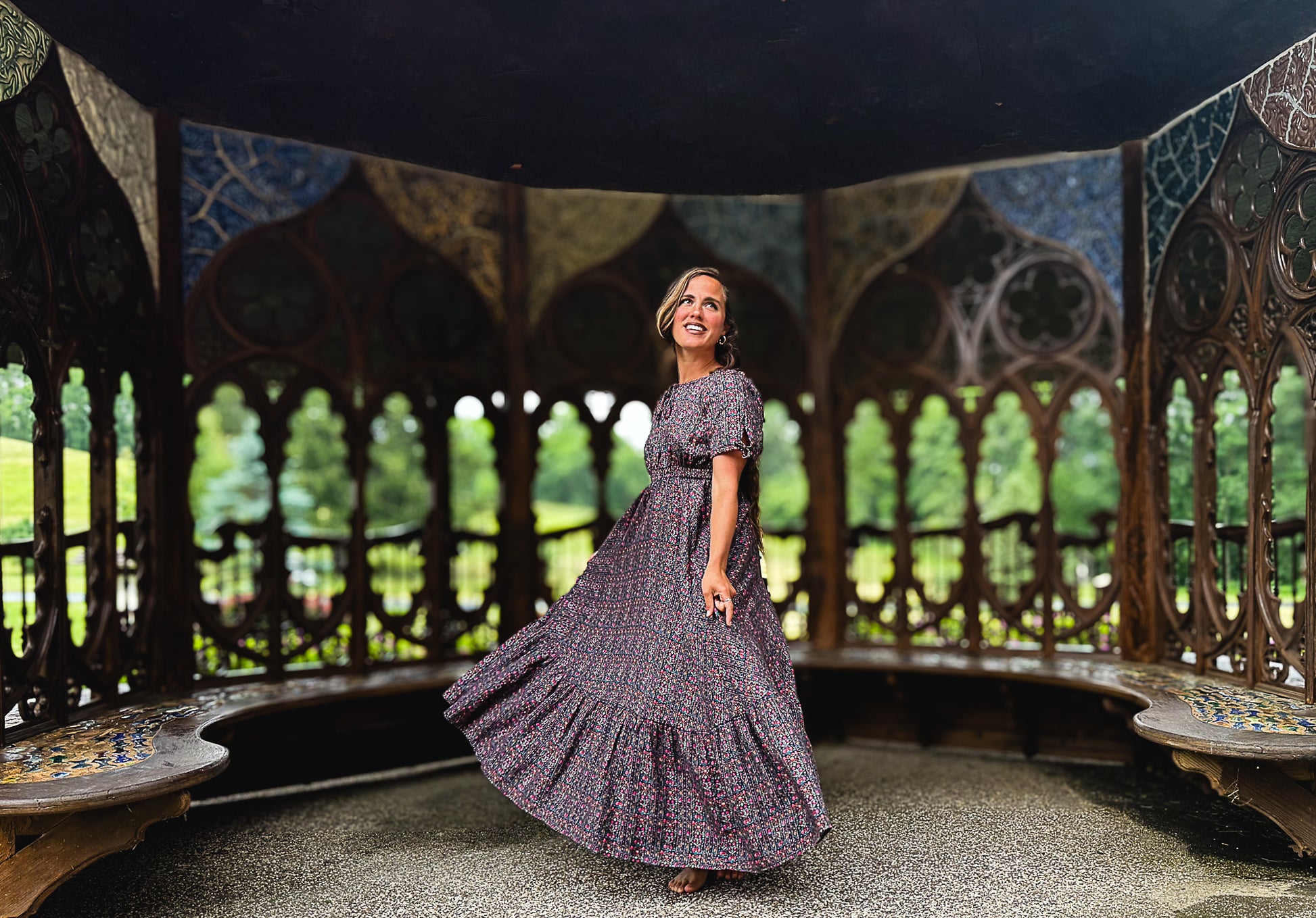 Woman in a long, patterned modest nursing dress standing in an ornate gazebo with mosaic walls.