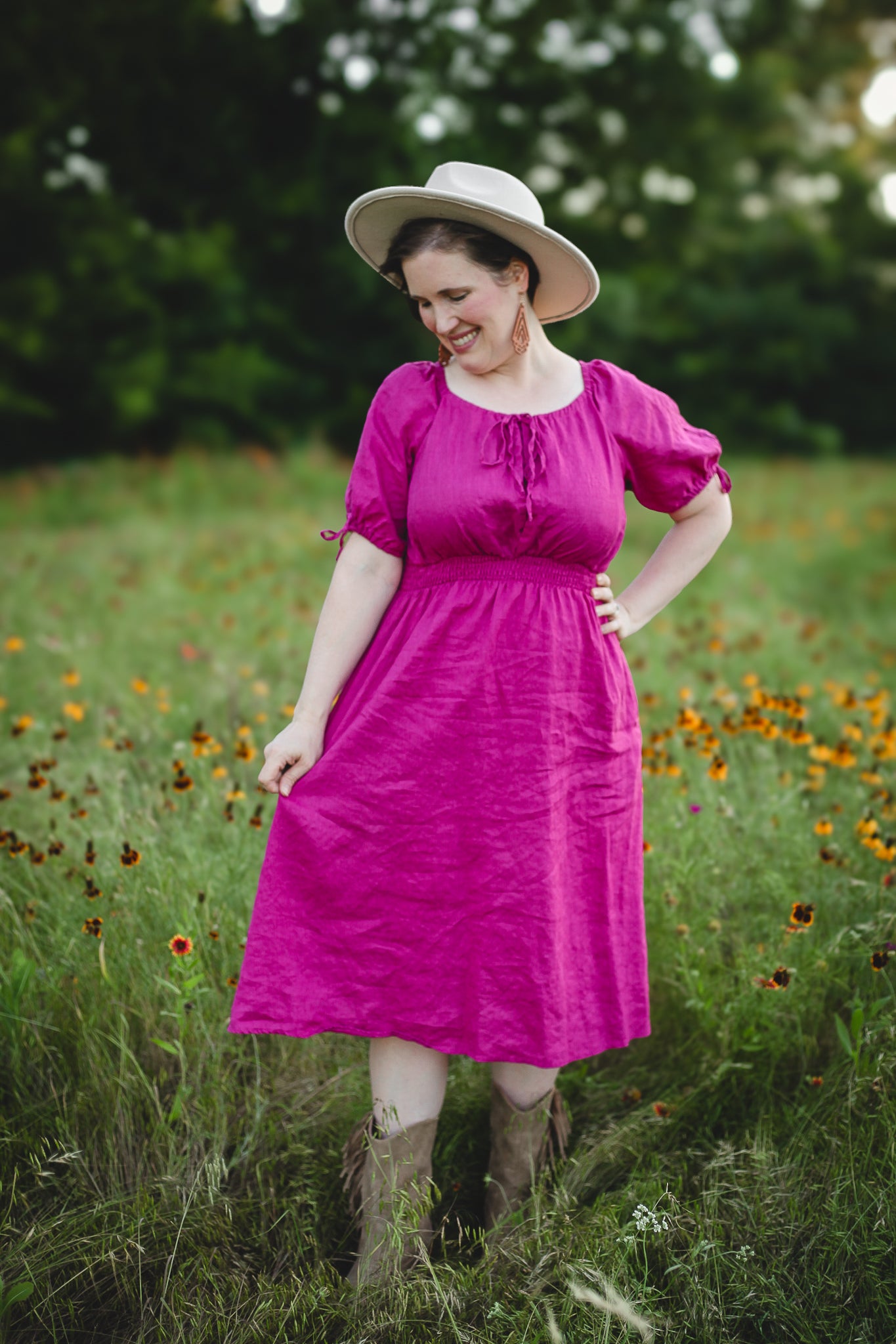 Woman in a pink modest nursing dress and hat standing in a field with wildflowers