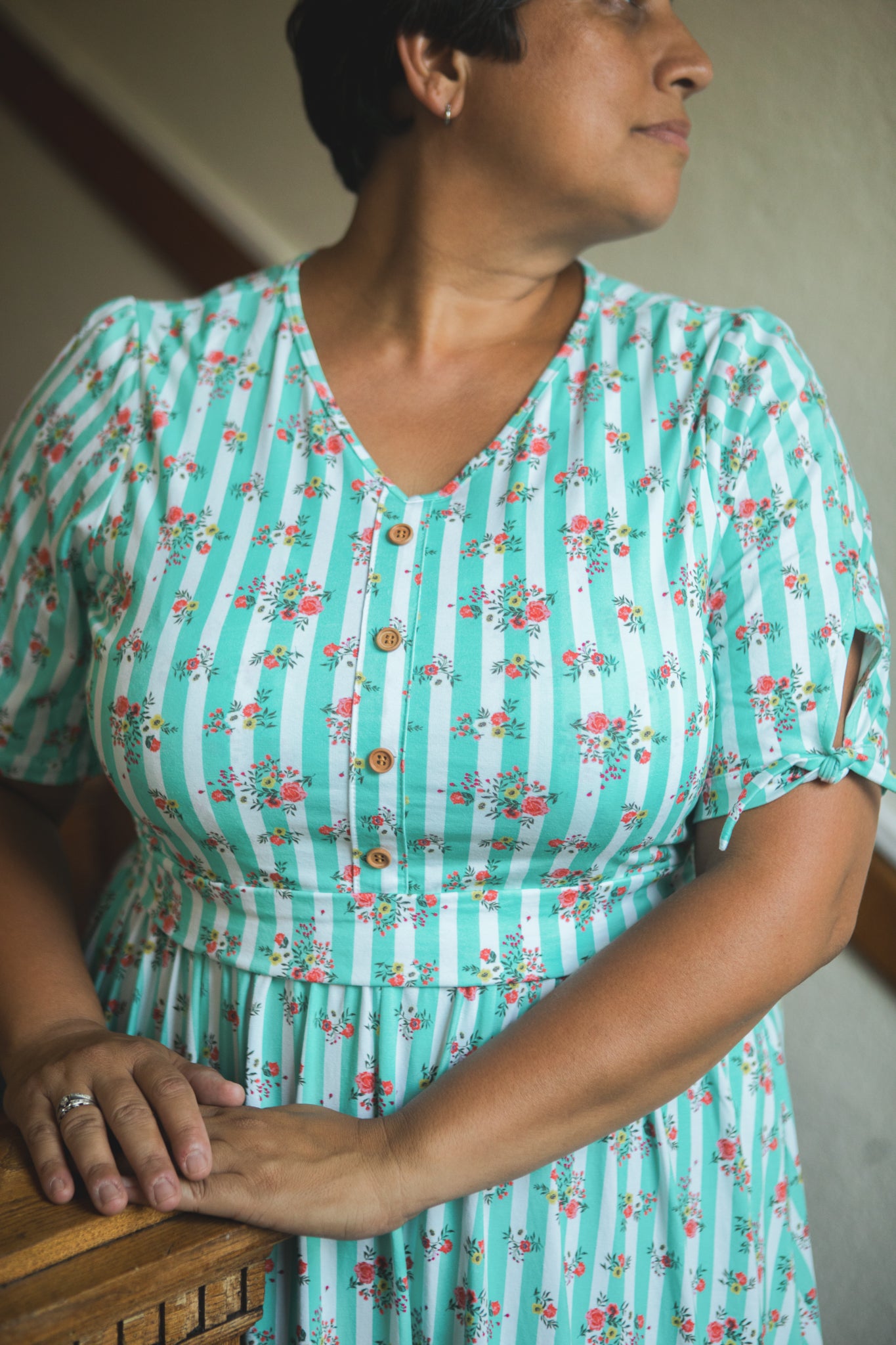 Woman wearing a teal modest nursing dress with floral and striped pattern, standing indoors.