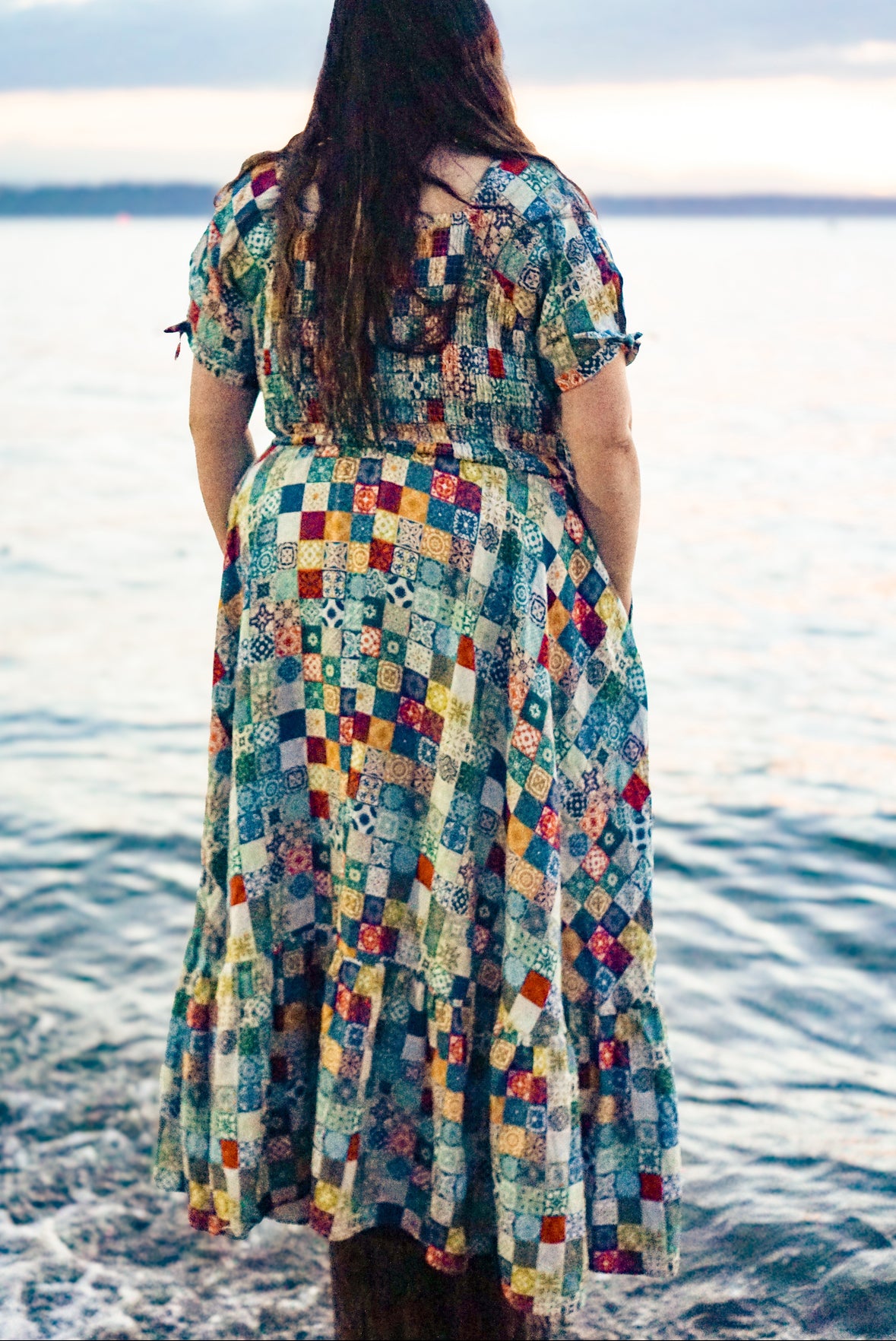 Person wearing a colorful patterned modest nursing dress standing by the water.
