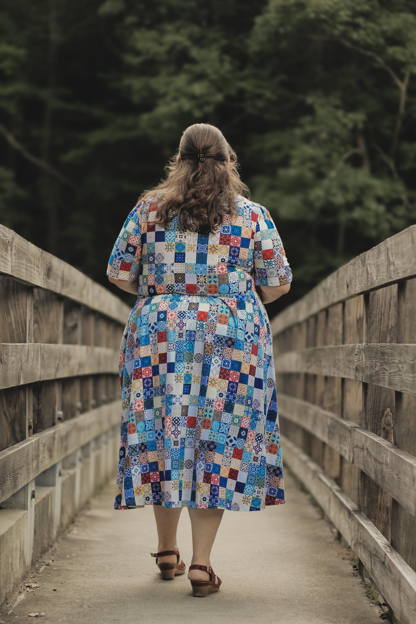 Woman in a colorful modest nursing dress walking on a wooden bridge with trees in the background