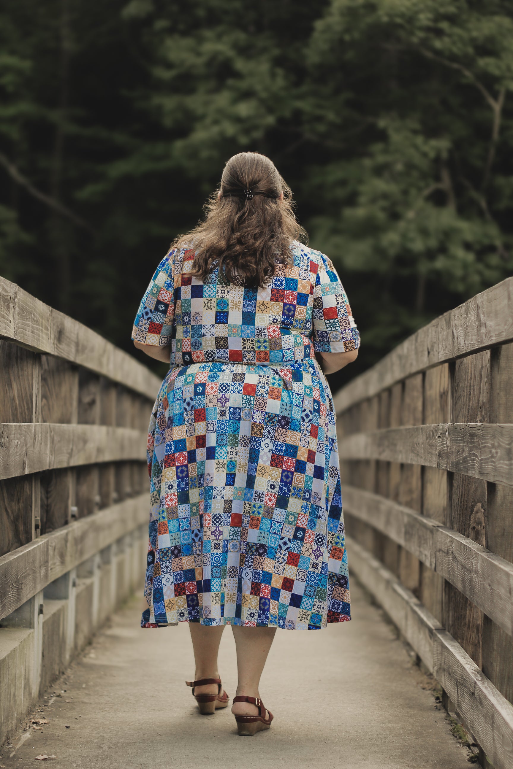 Woman in a colorful modest nursing dress walking on a wooden bridge with trees in the background