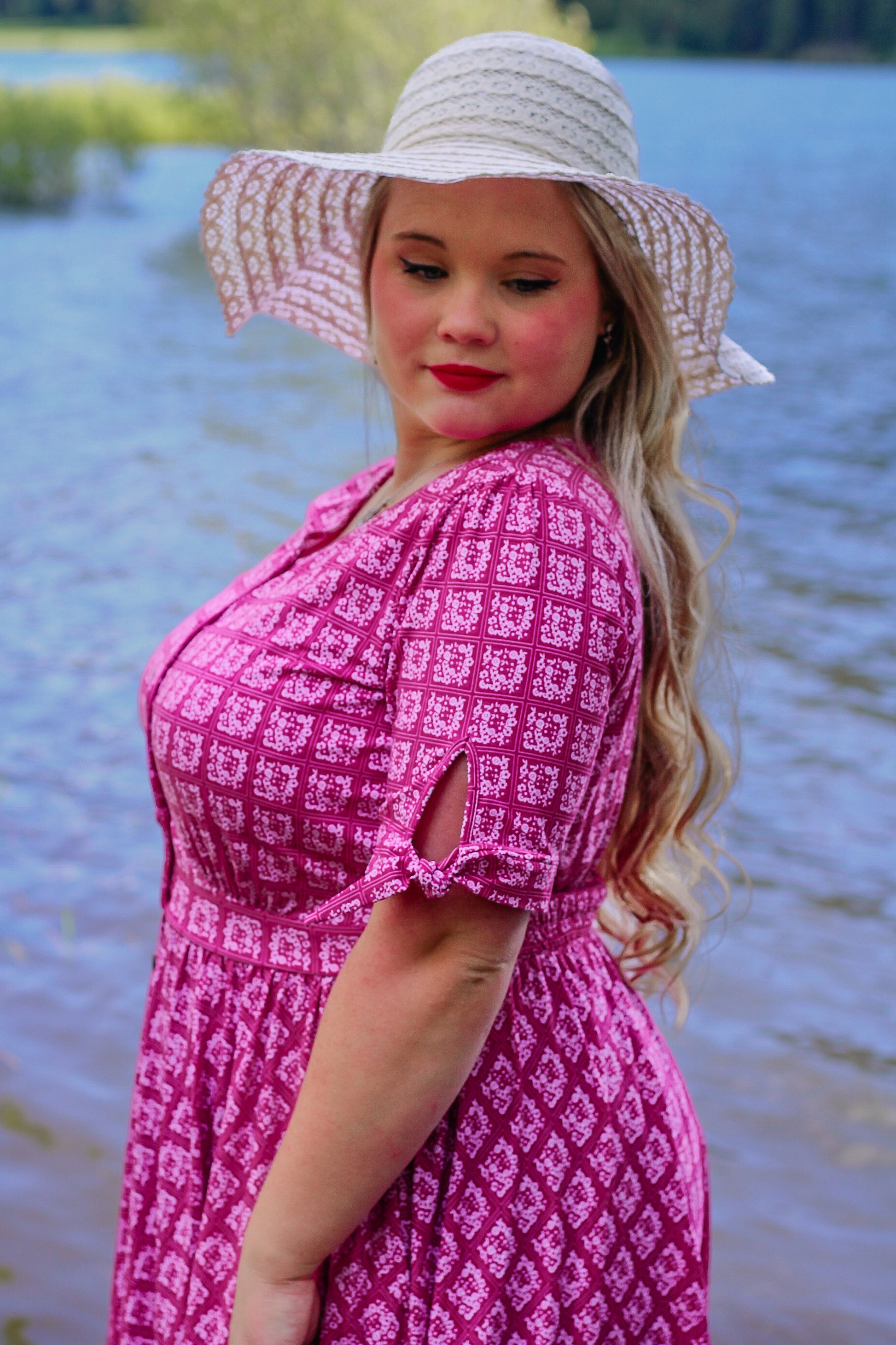 Woman in a pink modest nursing dress and white sun hat by a body of water