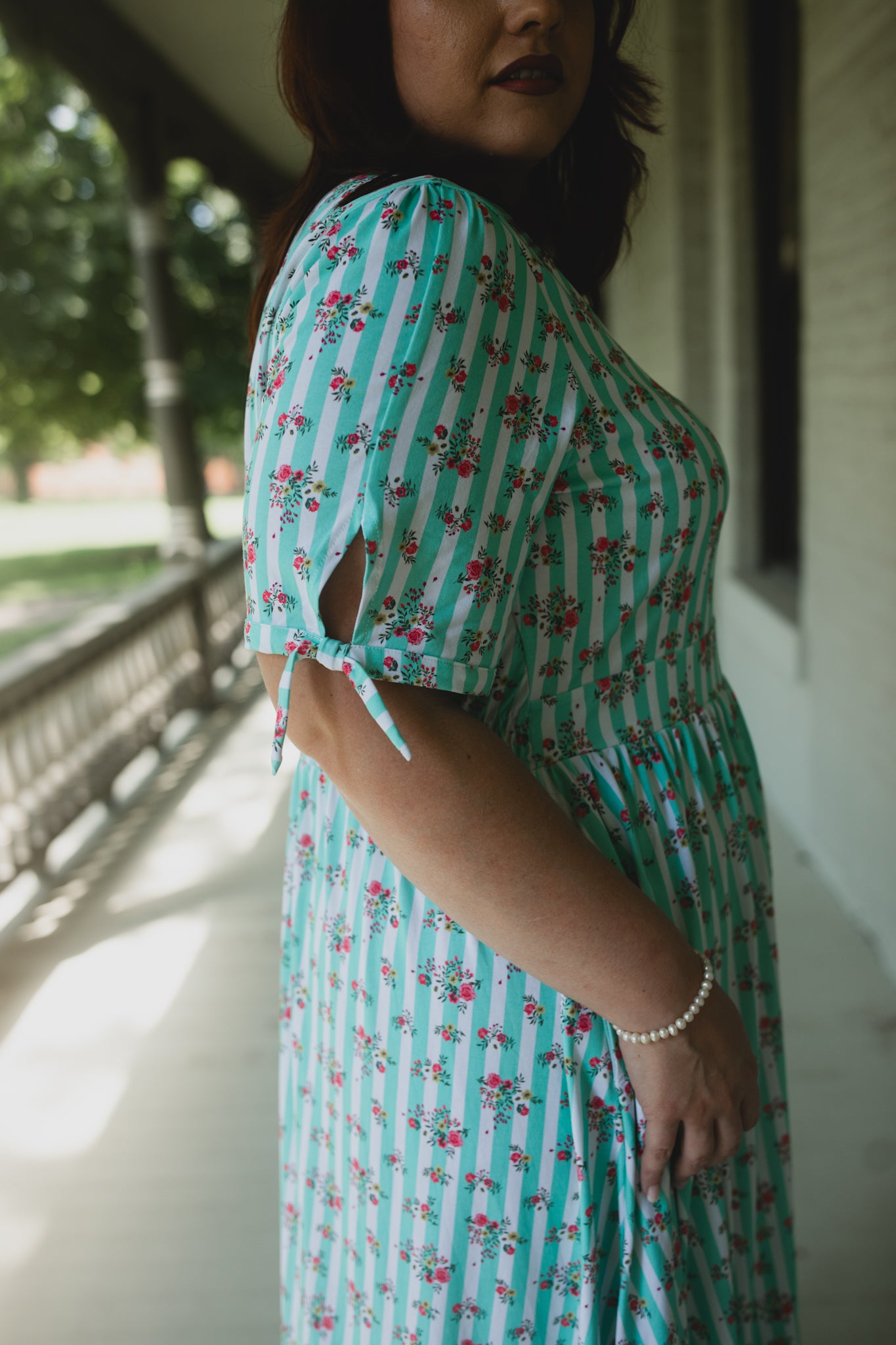 Woman wearing a green floral modest nursing dress on a blurred outdoor background