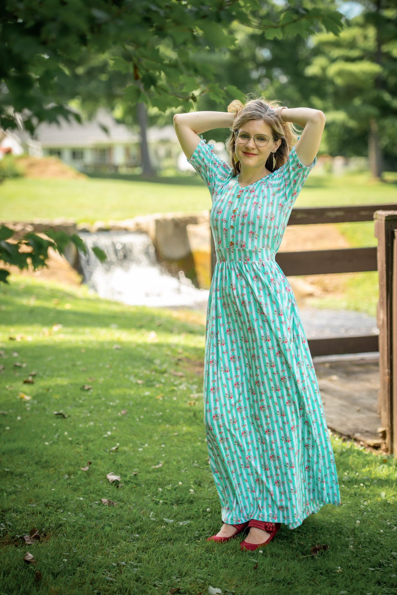 Woman in a green patterned modest nursing dress standing outdoors with trees and grass in the background
