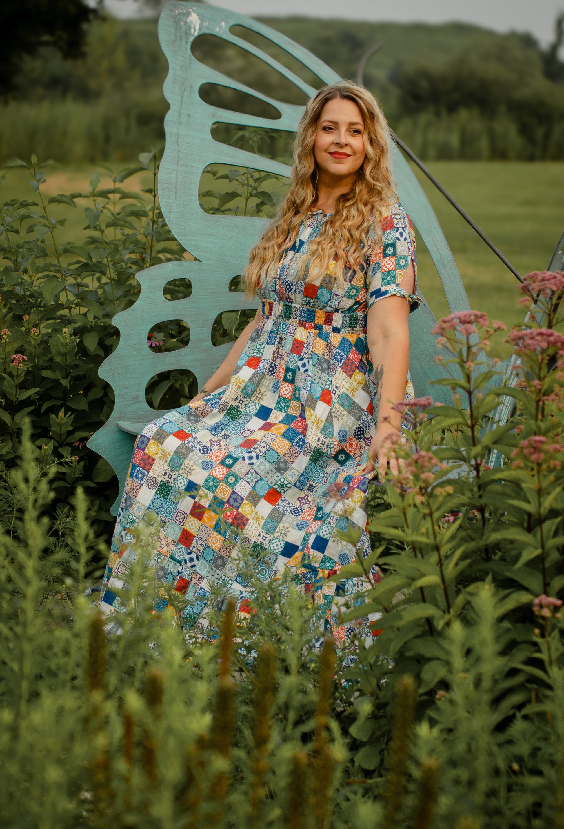 Woman in a colorful modest nursing dress sitting on a large butterfly-shaped chair in a field.
