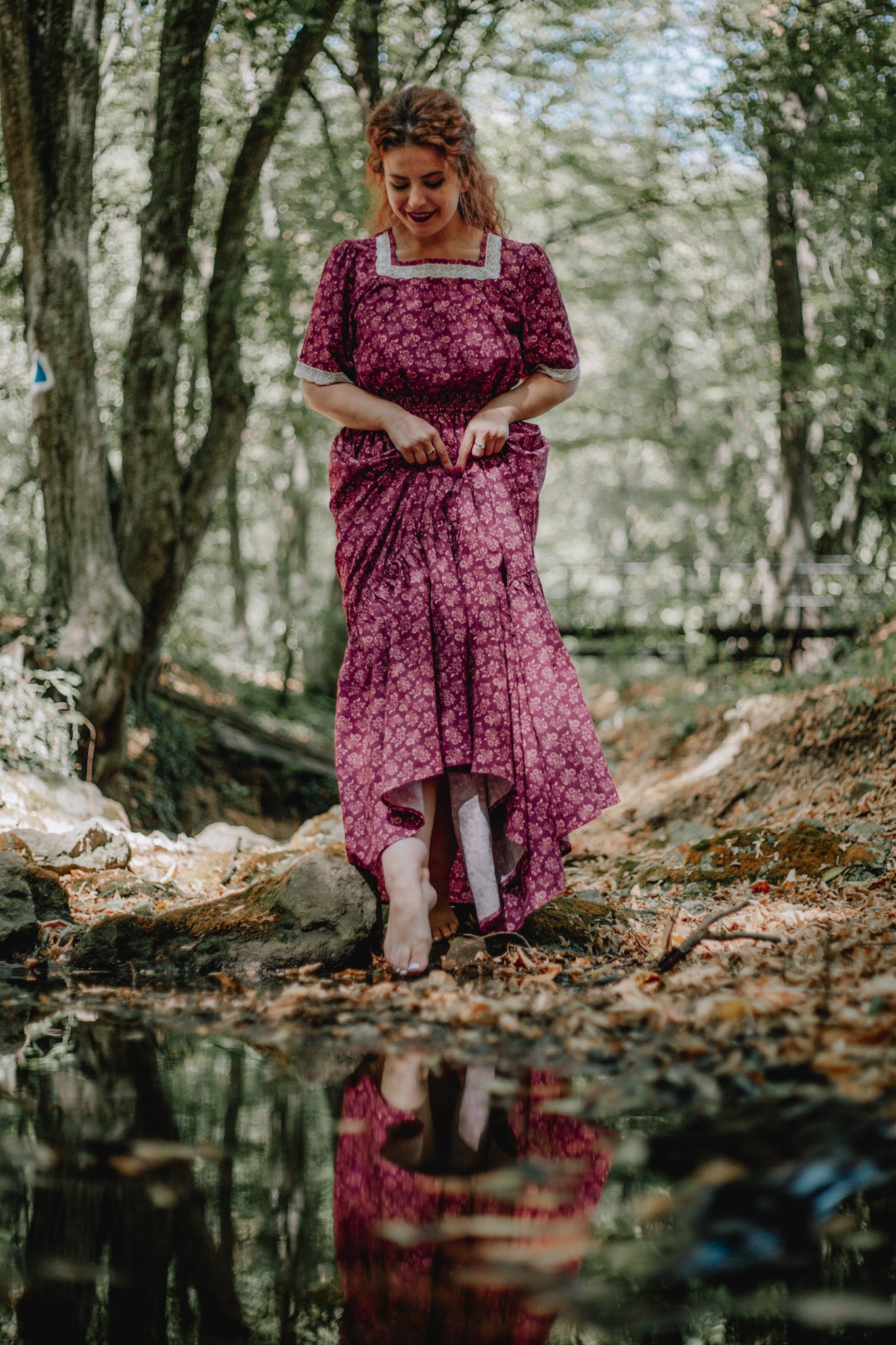 Woman in modest purple nursing dress by forest stream
