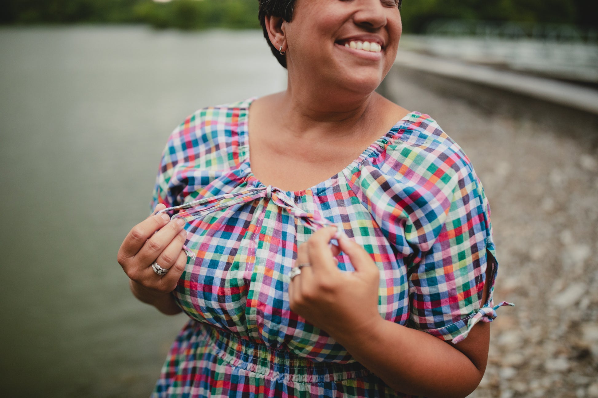 Woman in a colorful checkered modest nursing dress standing by a body of water.