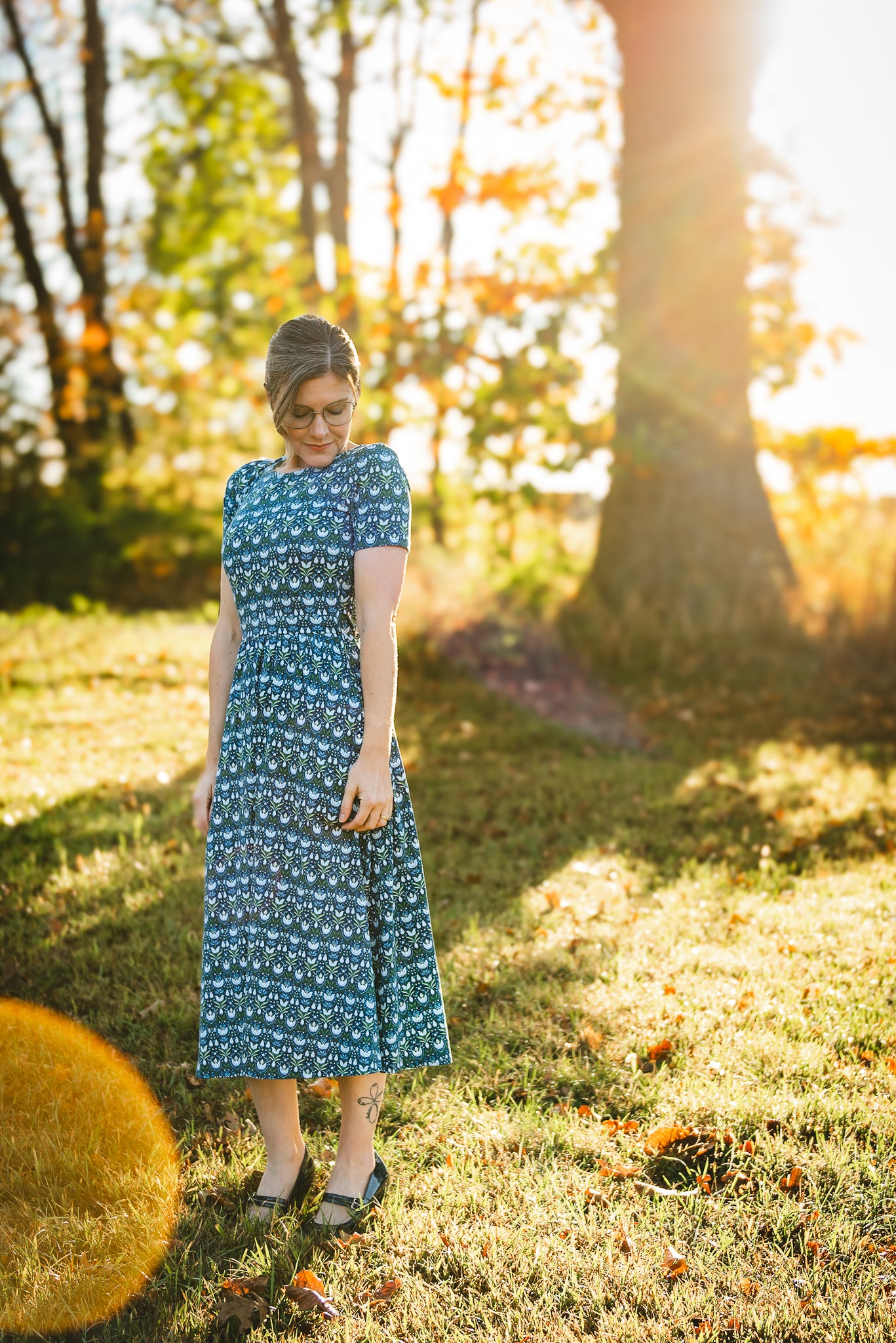 Woman in modest nursing dress, sunlit field trees.