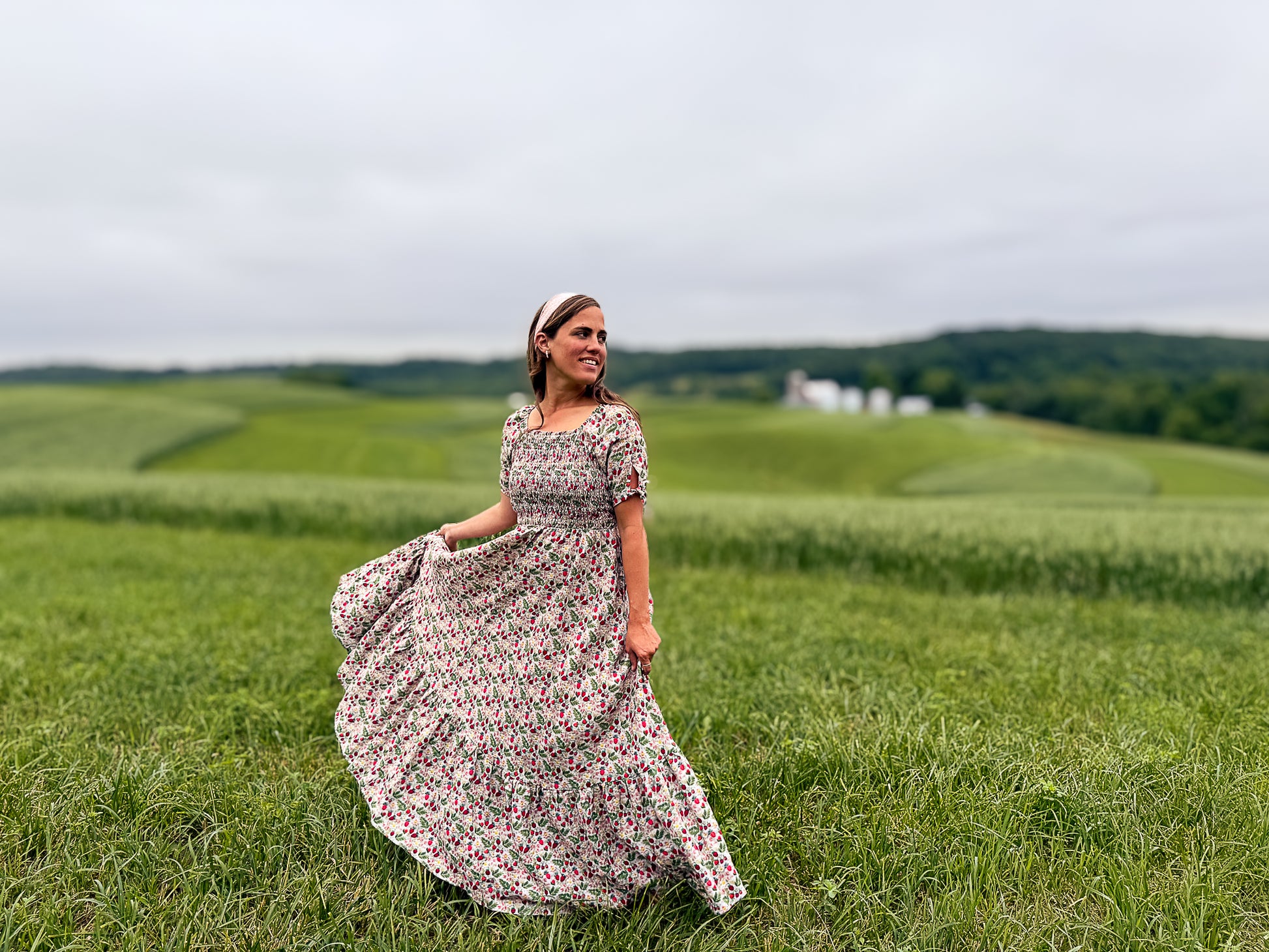Woman in a floral modest nursing dress standing in a green field with rolling hills in the background