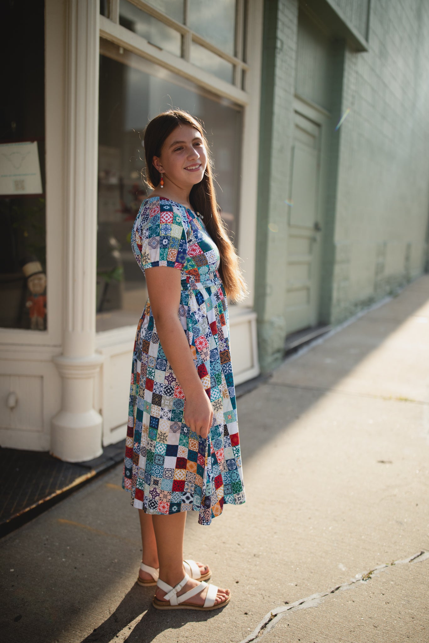 Woman wearing a colorful patchwork modest nursing dress standing on a sidewalk.