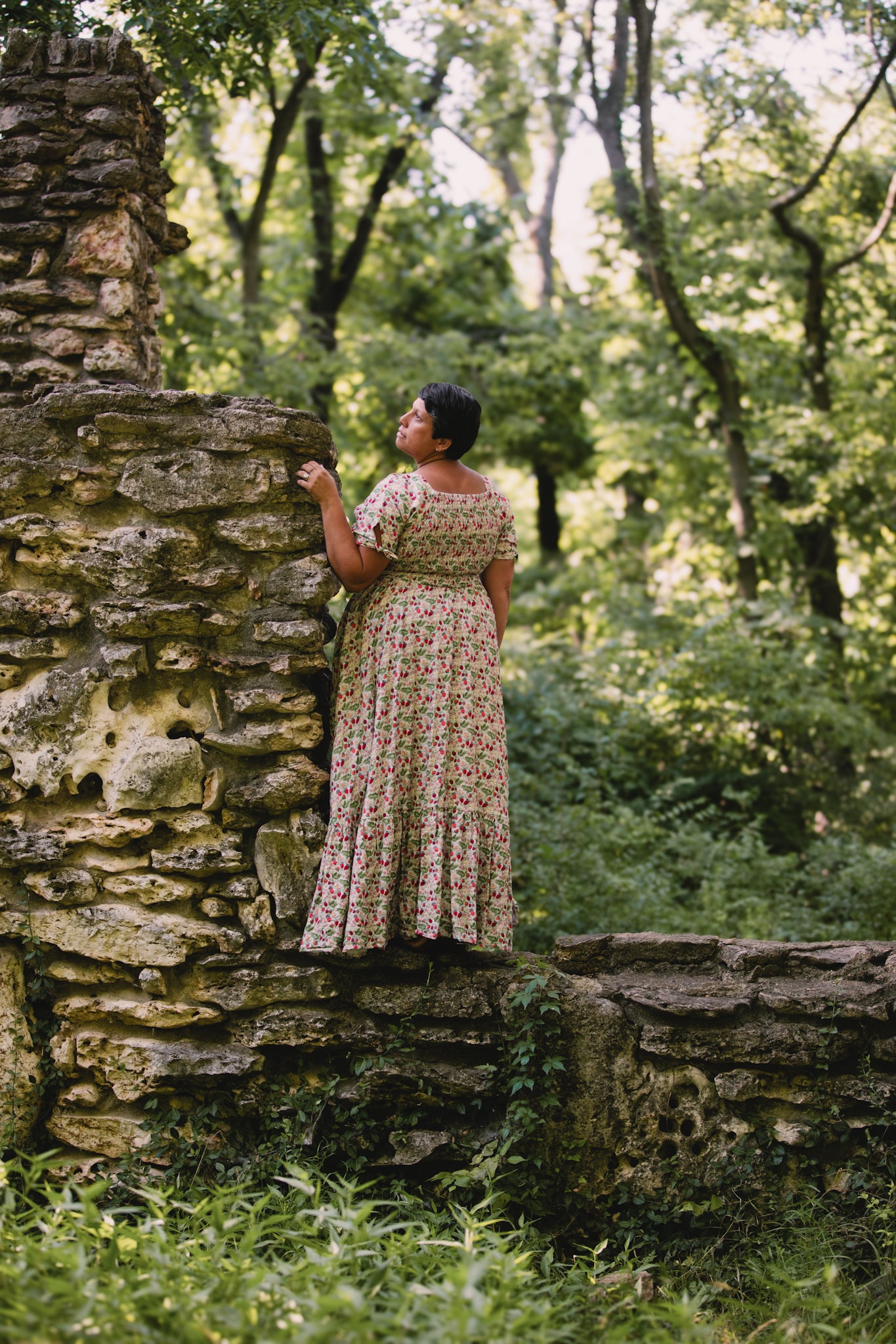 Woman in a floral modest nursing dress standing on a stone wall in a forest