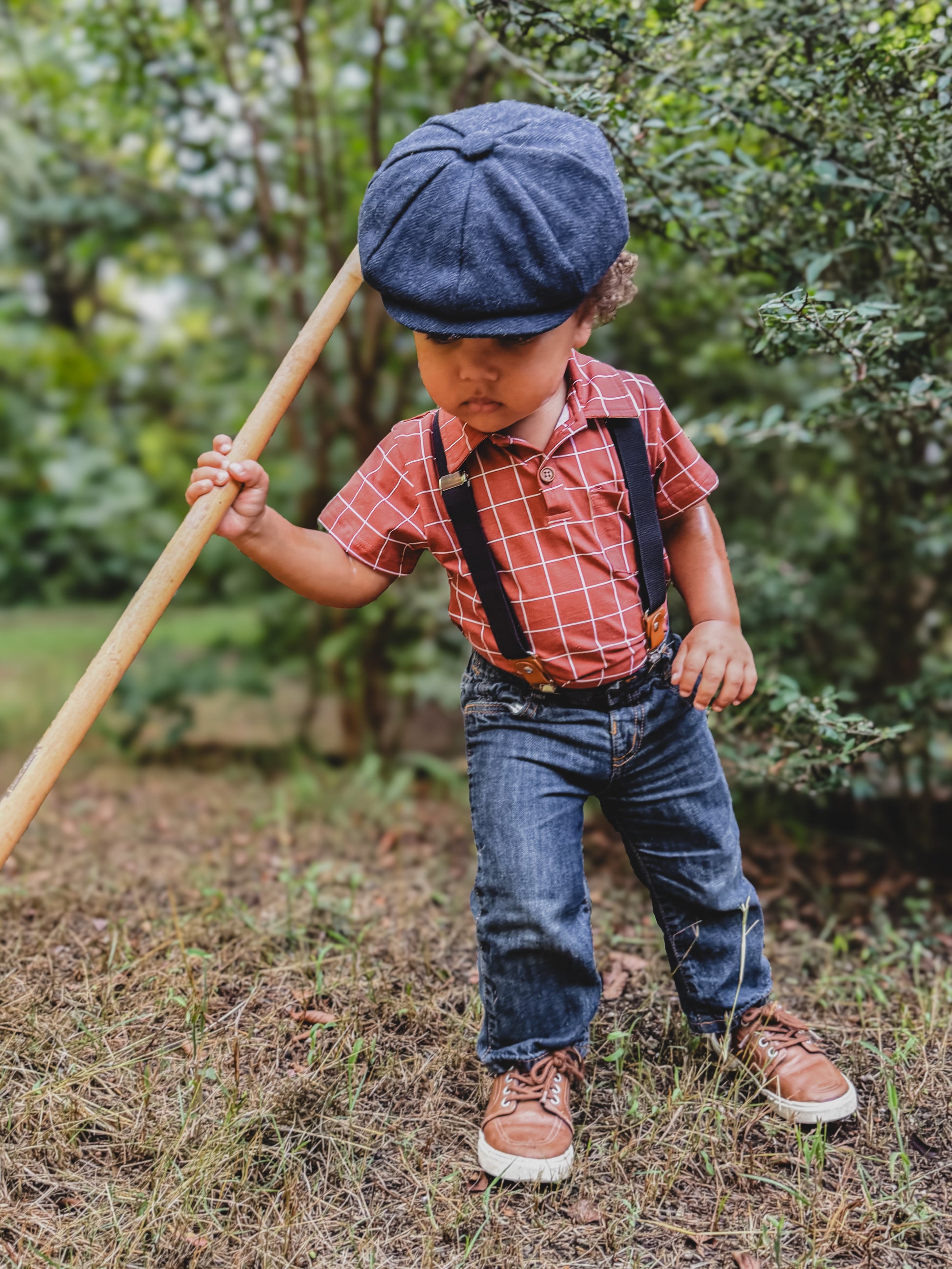 Boy in plaid shirt with suspenders holding stick