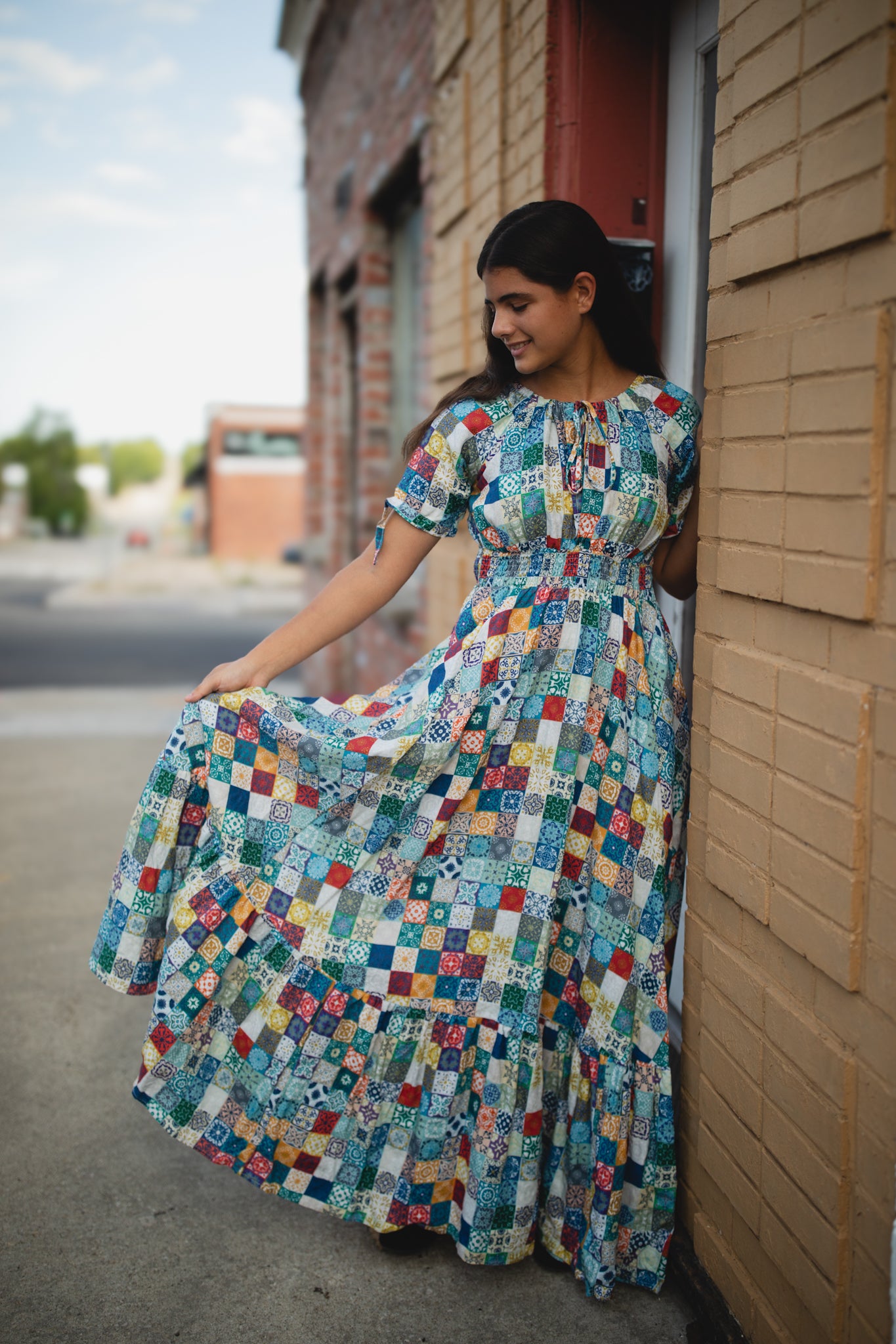 Woman in a colorful patterned modest nursing dress standing against a brick wall.