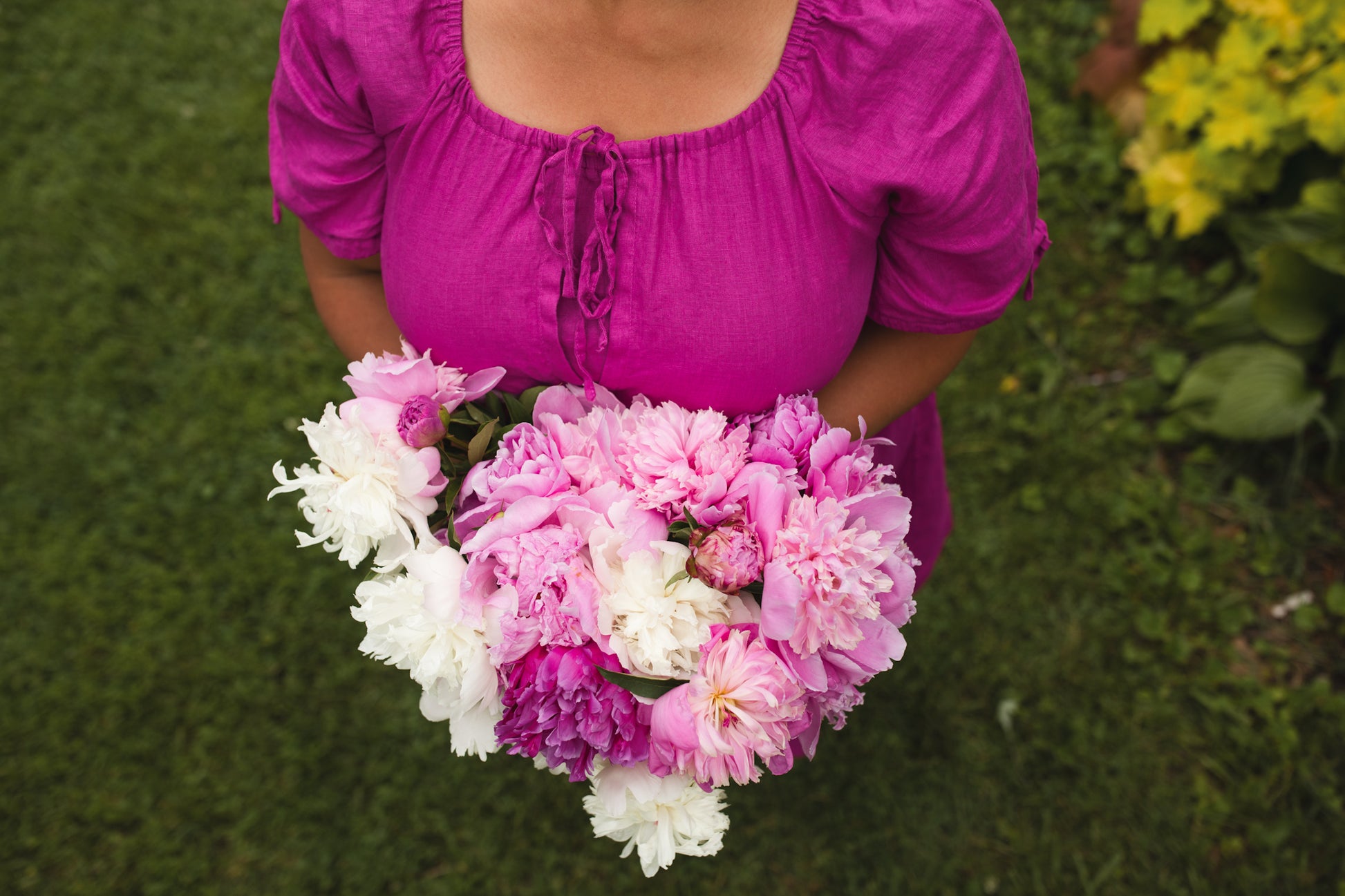 Person holding a heart-shaped bouquet of pink and white flowers against a green grass background wearing a modest nursing dress
