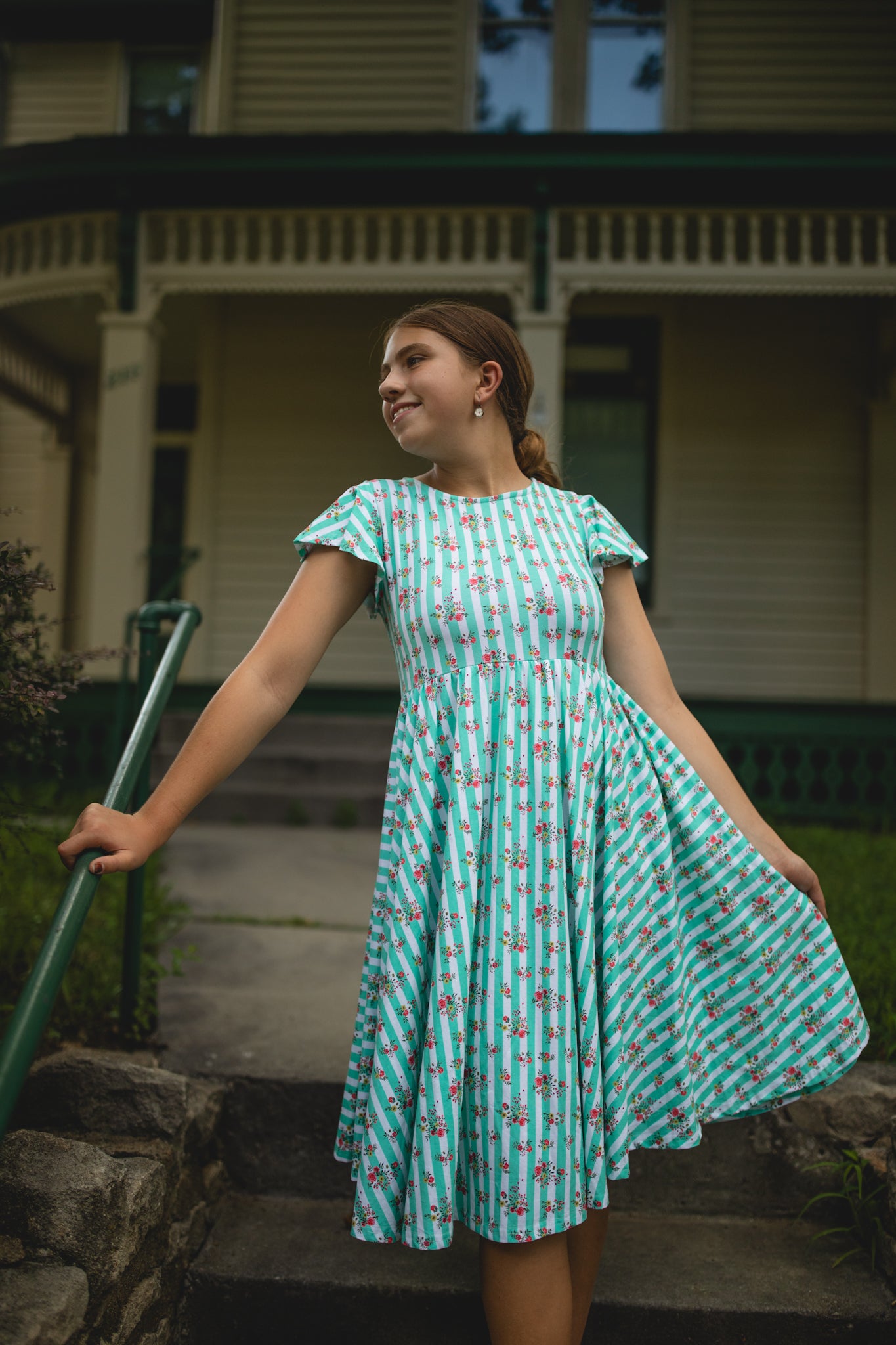 Woman in a floral modest dress standing outdoors with a house in the background