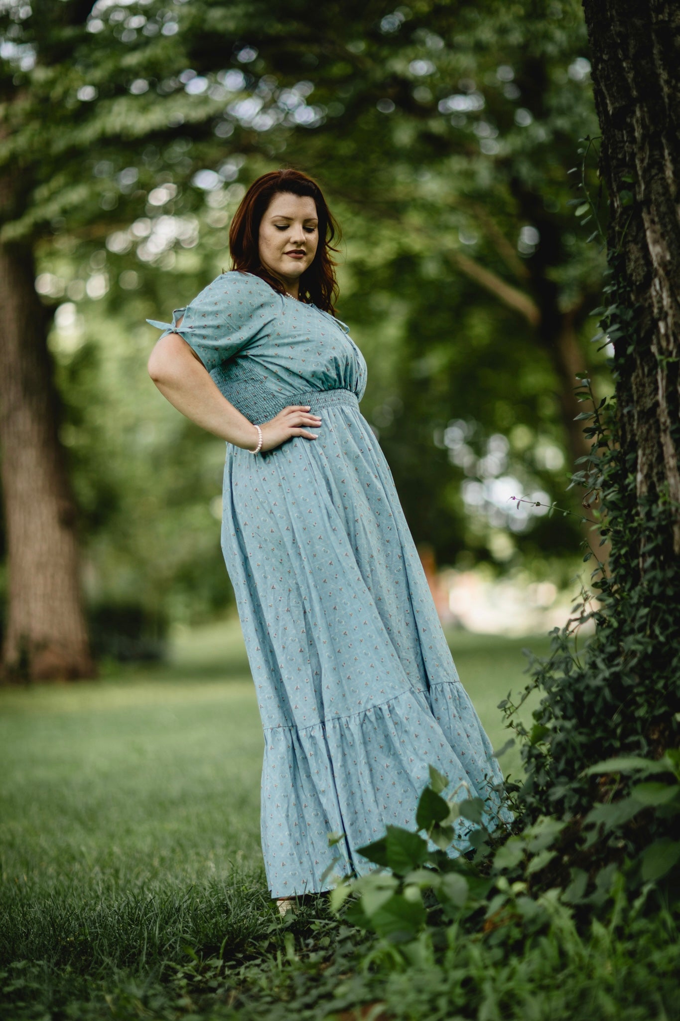 Woman in a light blue modest nursing dress standing outdoors among trees and greenery