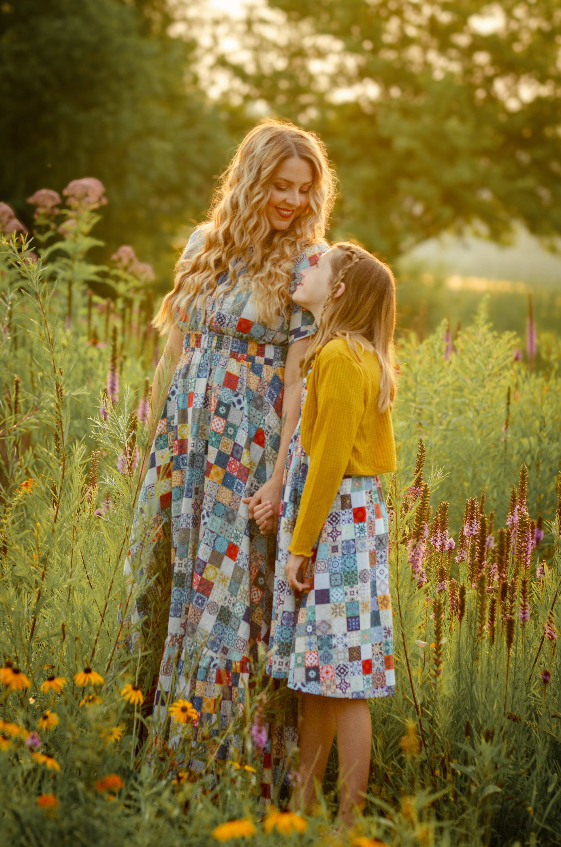 Woman and young girl standing in a field of flowers, both wearing colorful modest dresses.