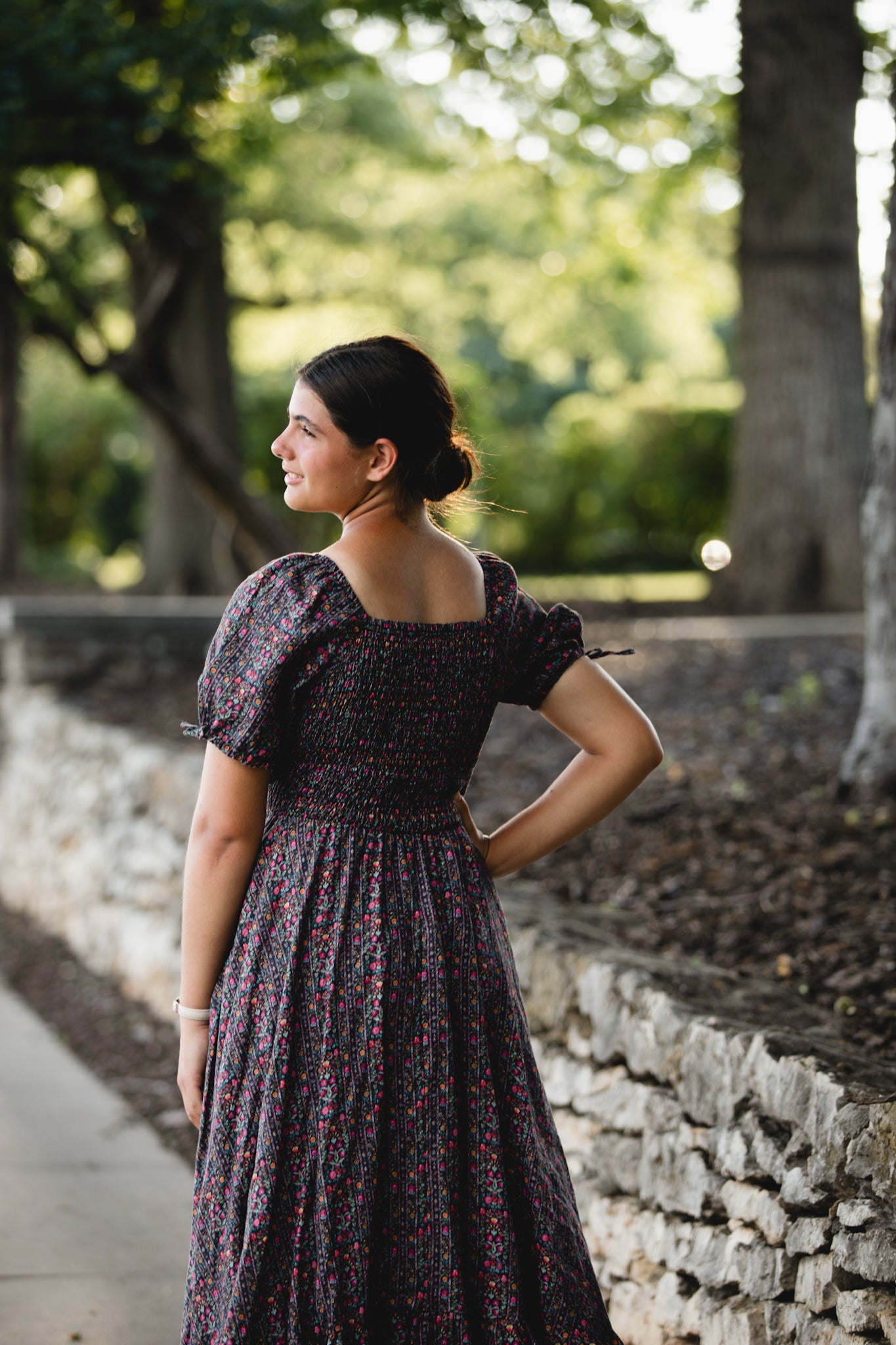 Woman in a dark floral modest nursing dress standing outdoors with greenery in the background