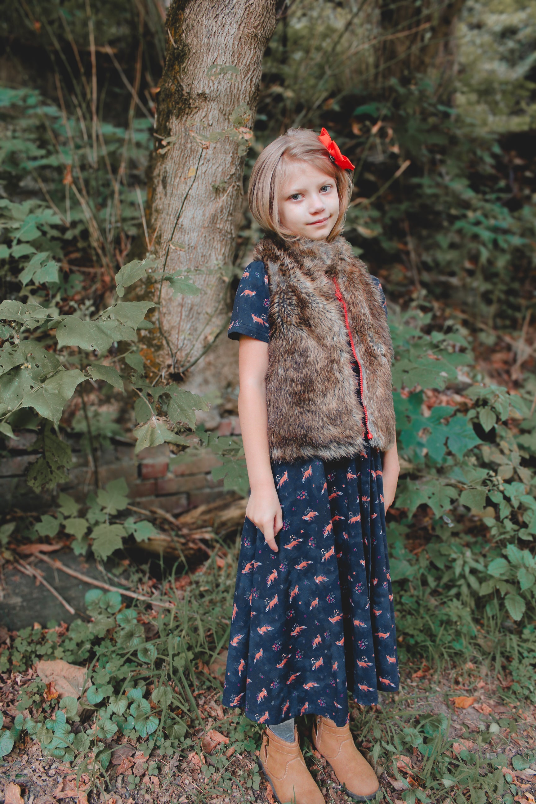 Young girl in modest navy dress with red bow wearing fur vest in forest