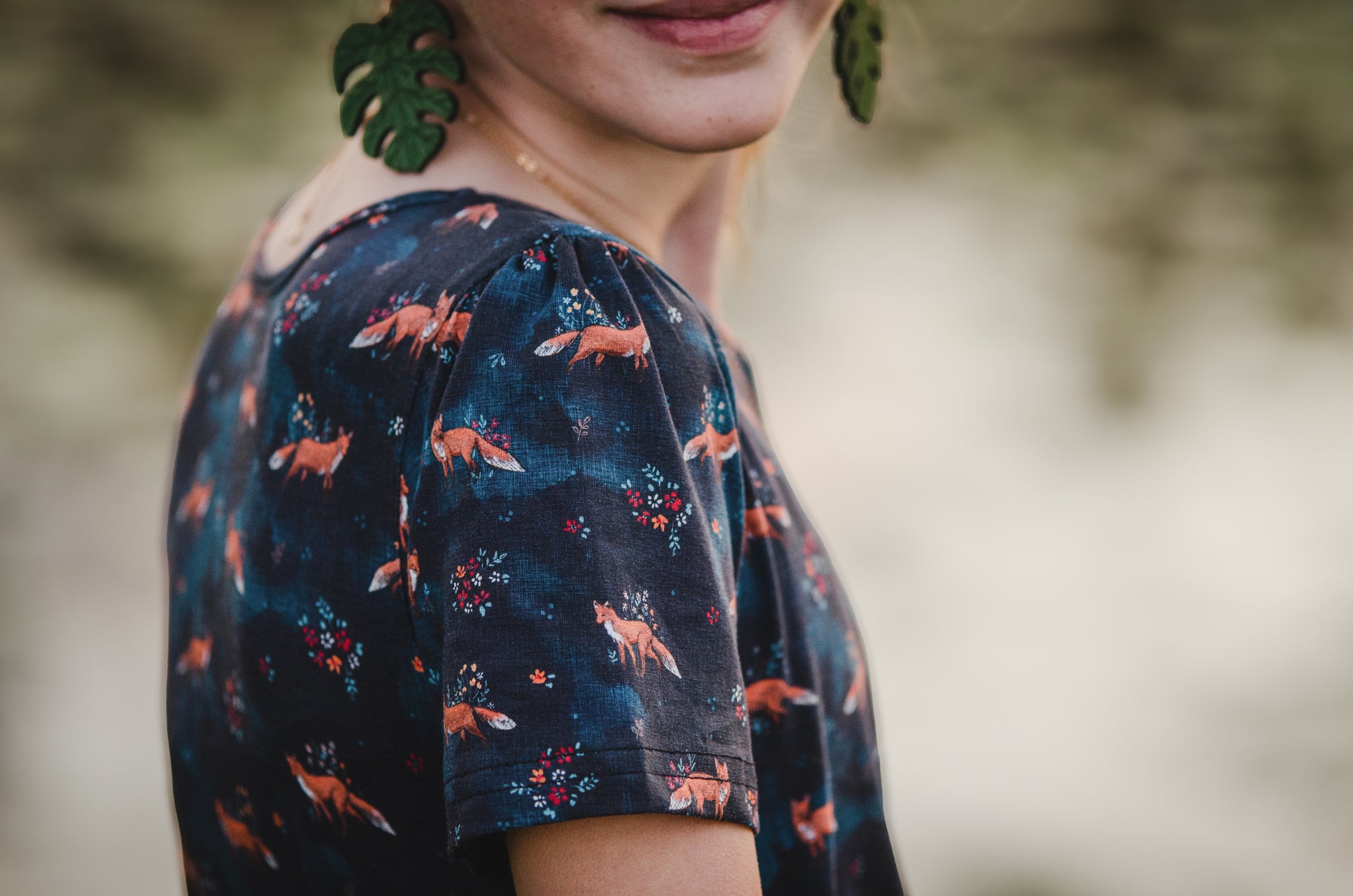 Person wearing modest dark blue fox-patterned dress against blurred natural background