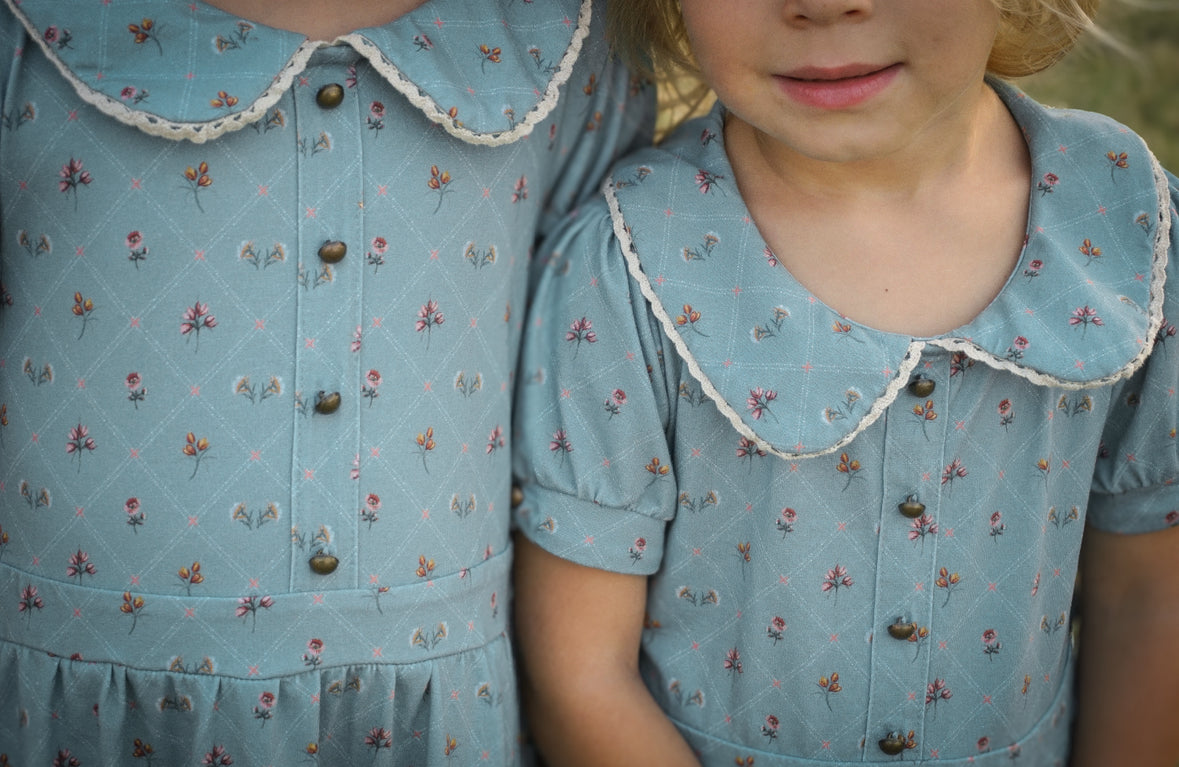 Two children wearing matching blue floral dresses with a close-up of the collars.