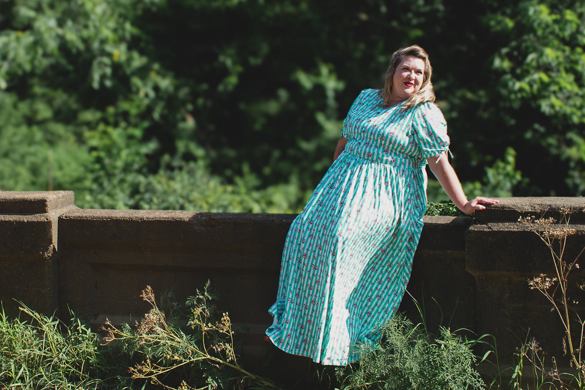 Woman in a blue modest dress standing outdoors with greenery in the background
