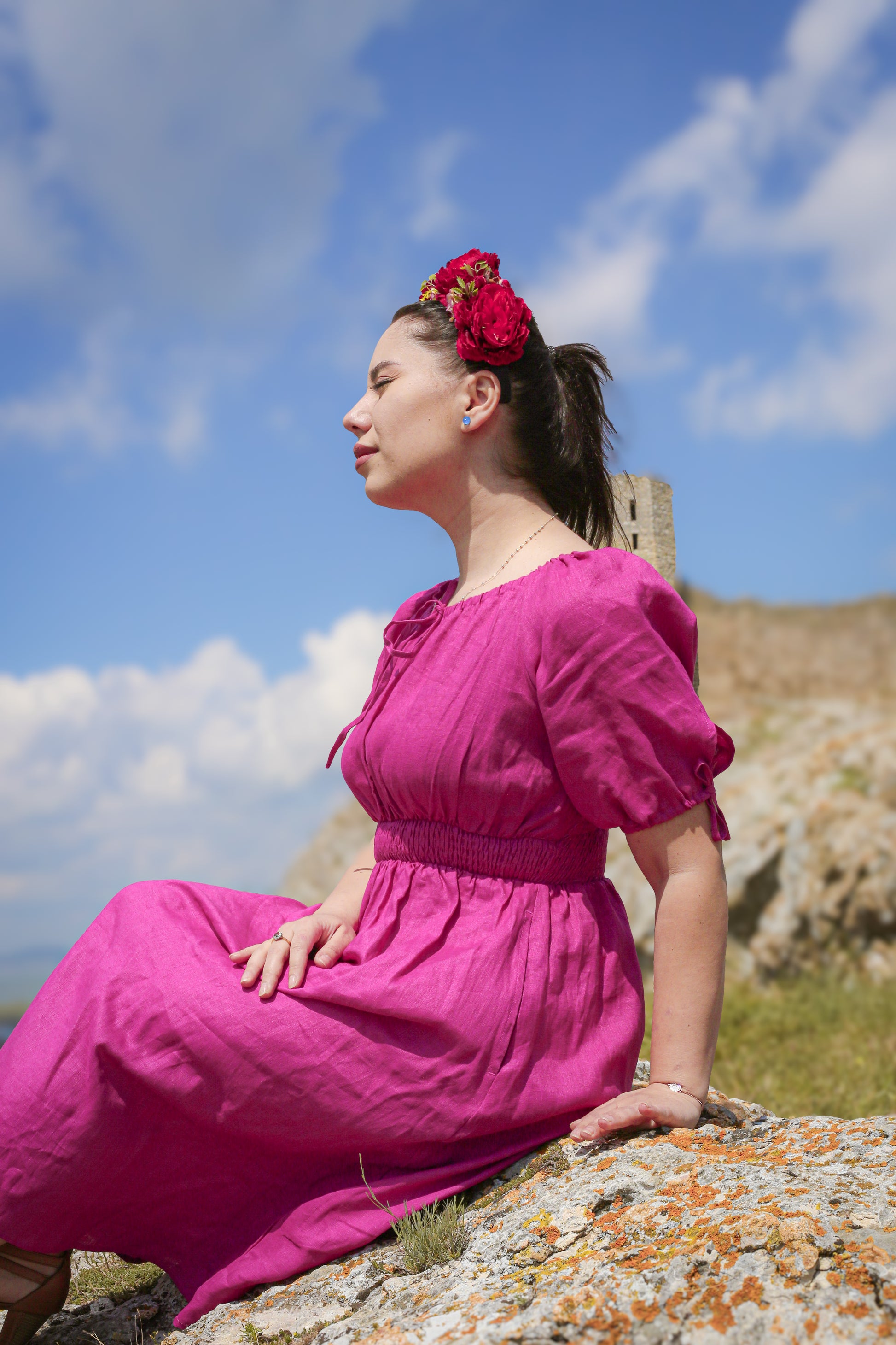 Woman in a pink modest nursing dress sitting on rocks with a castle in the background