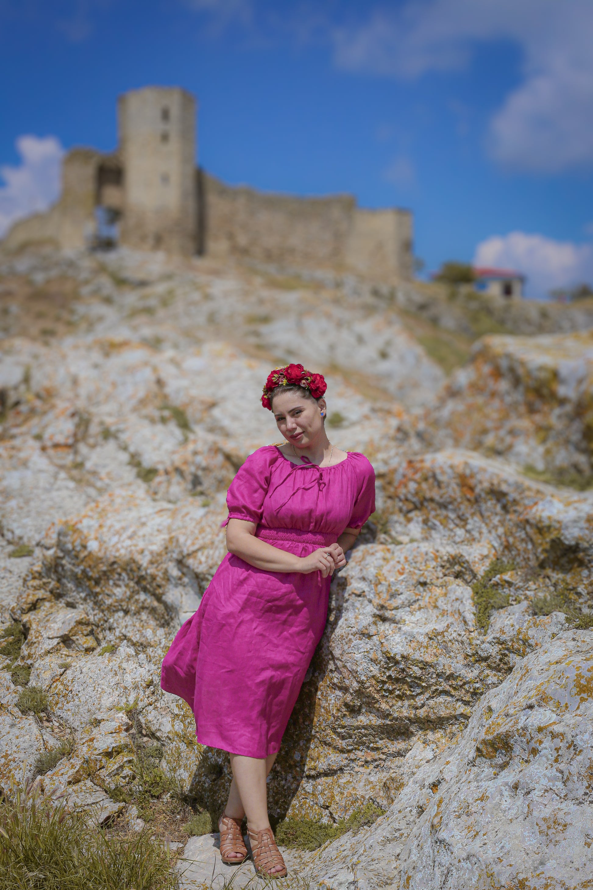 Woman in a pink modest nursing dress standing on rocky terrain with a castle in the background
