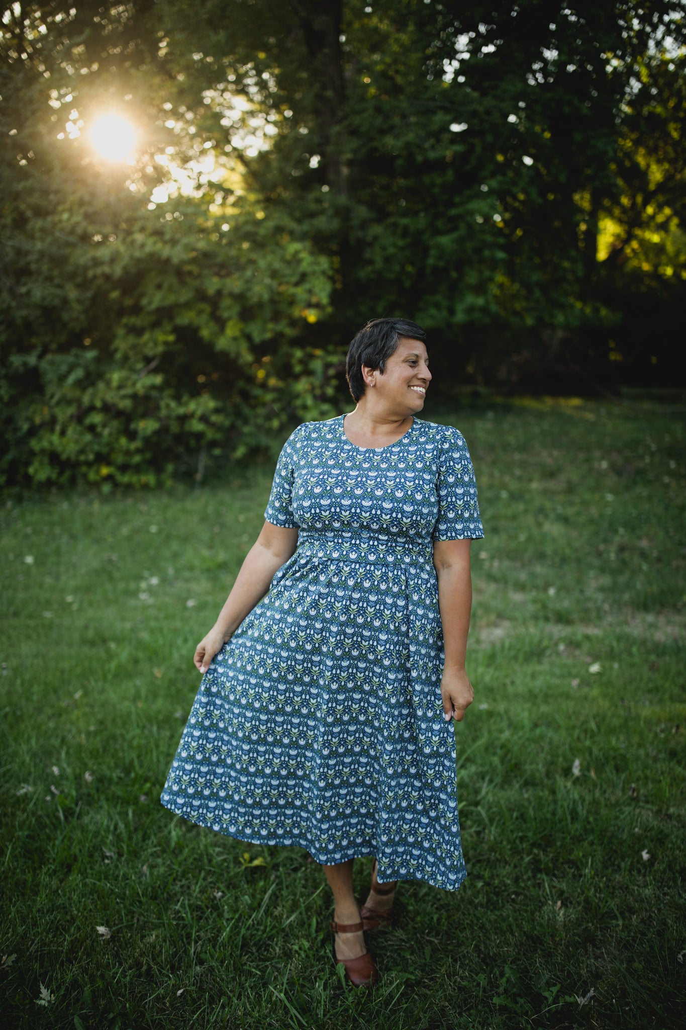 Woman in modest nursing dress, grassy trees.
