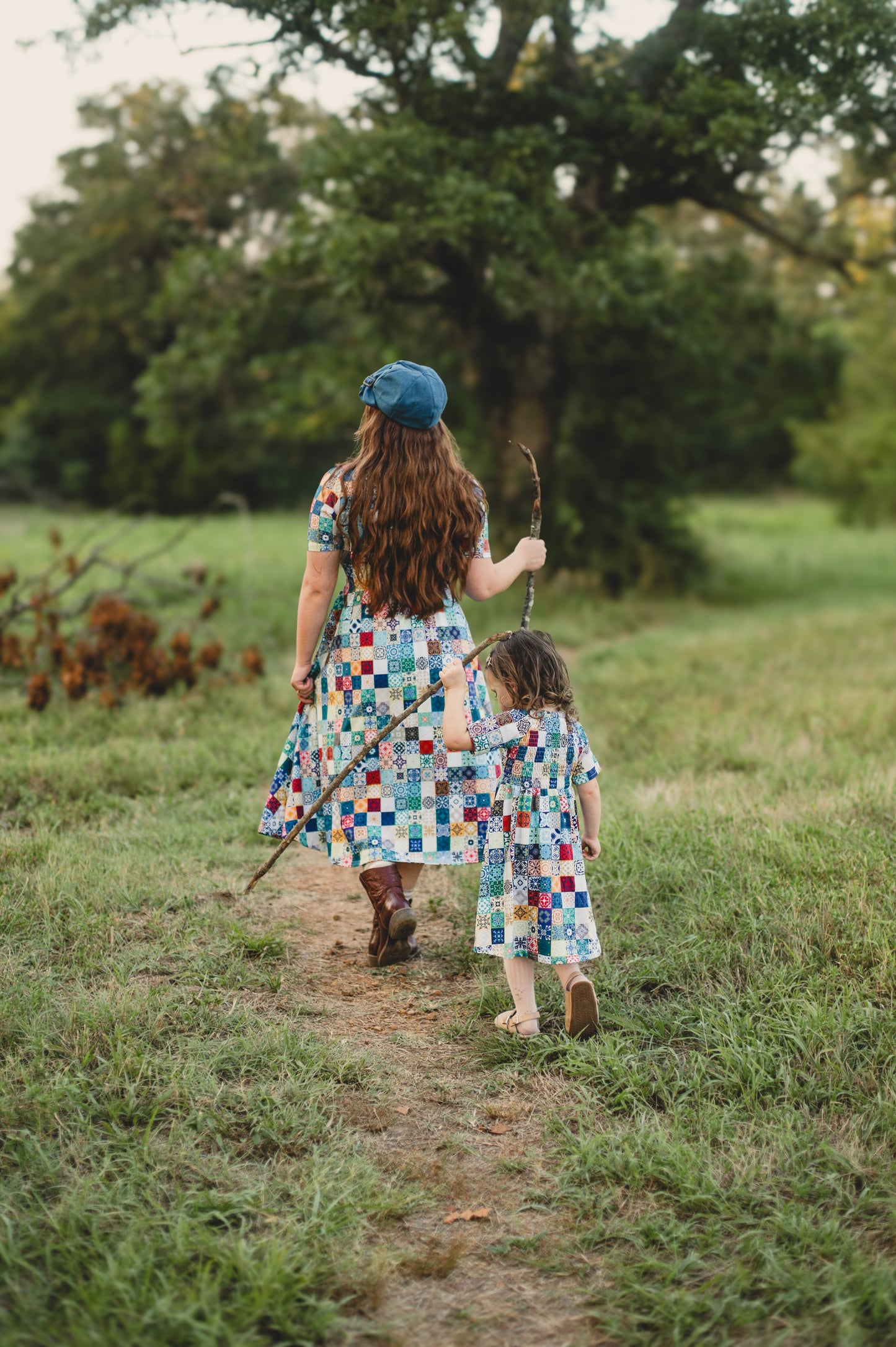 Mother and daughter in colorful modest dresses walking along a path in a natural setting.