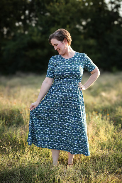 Woman in modest nursing dress, field with trees.