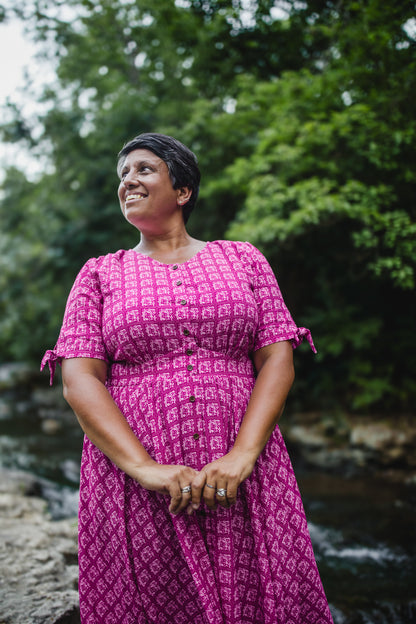 Woman in a pink modest nursing dress standing outdoors with greenery in the background