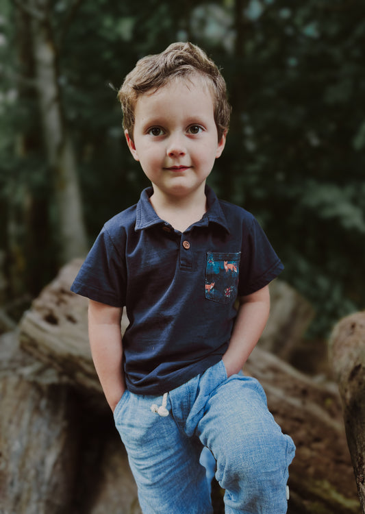 Boy in blue polo outdoors with trees.