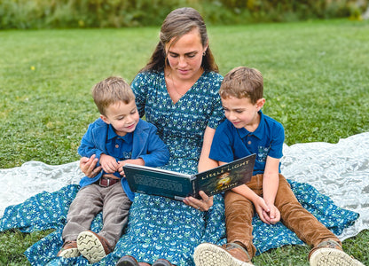 Mother in modest nursing dress reading to children outdoors