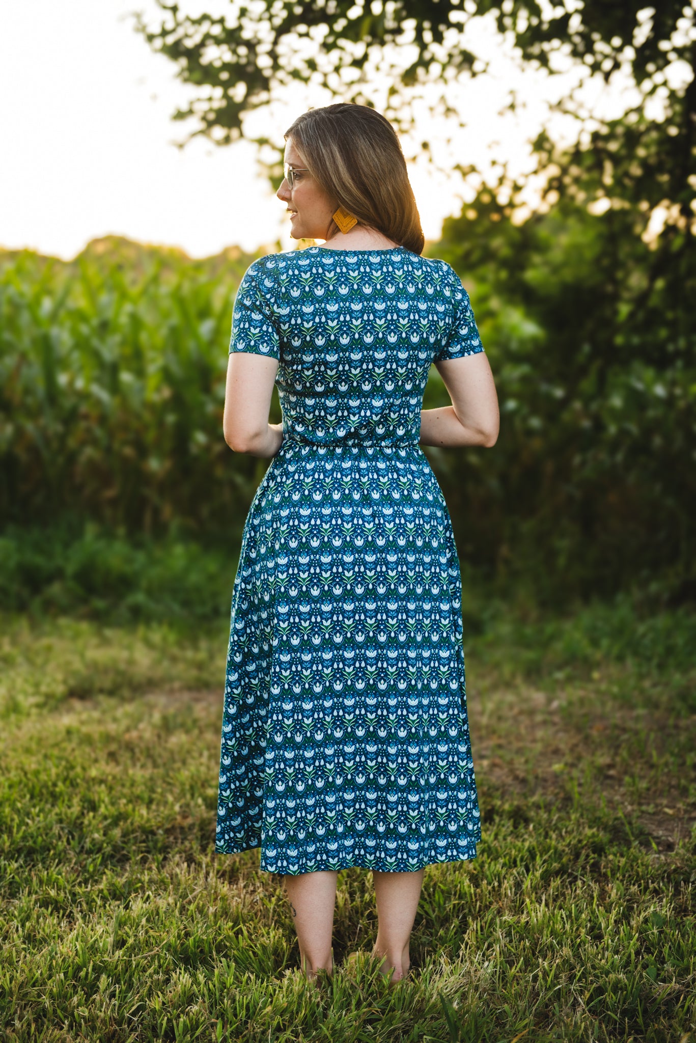 Woman in modest nursing dress, grassy field trees.