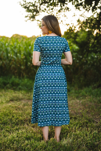 Woman in modest nursing dress, grassy field trees.