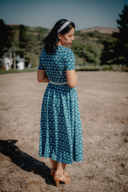 Woman in modest nursing dress outdoors with trees.