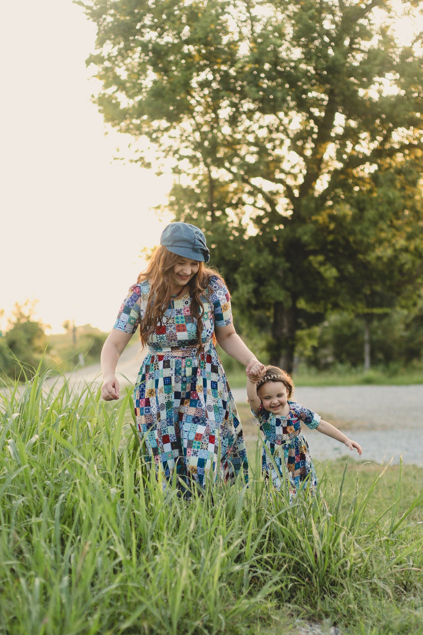 Mother and daughter walking through tall grass with trees in the background wearing modest dresses