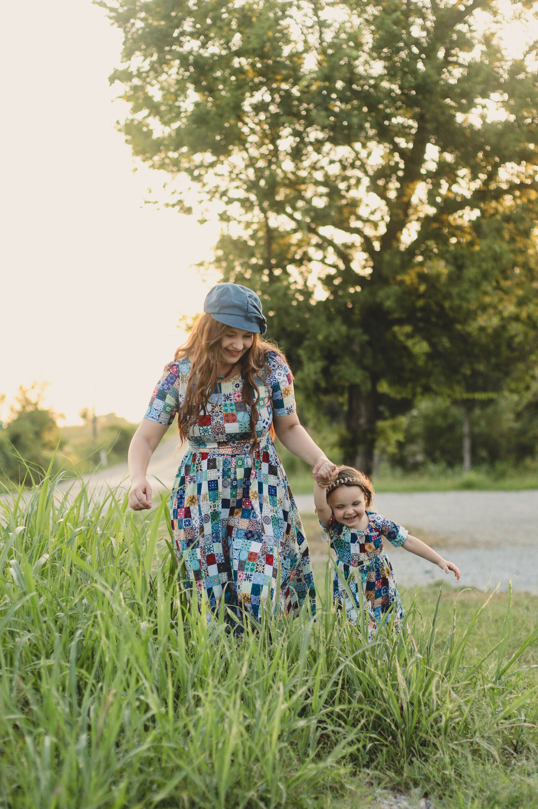 Mother and daughter walking through tall grass with trees in the background wearing modest dresses