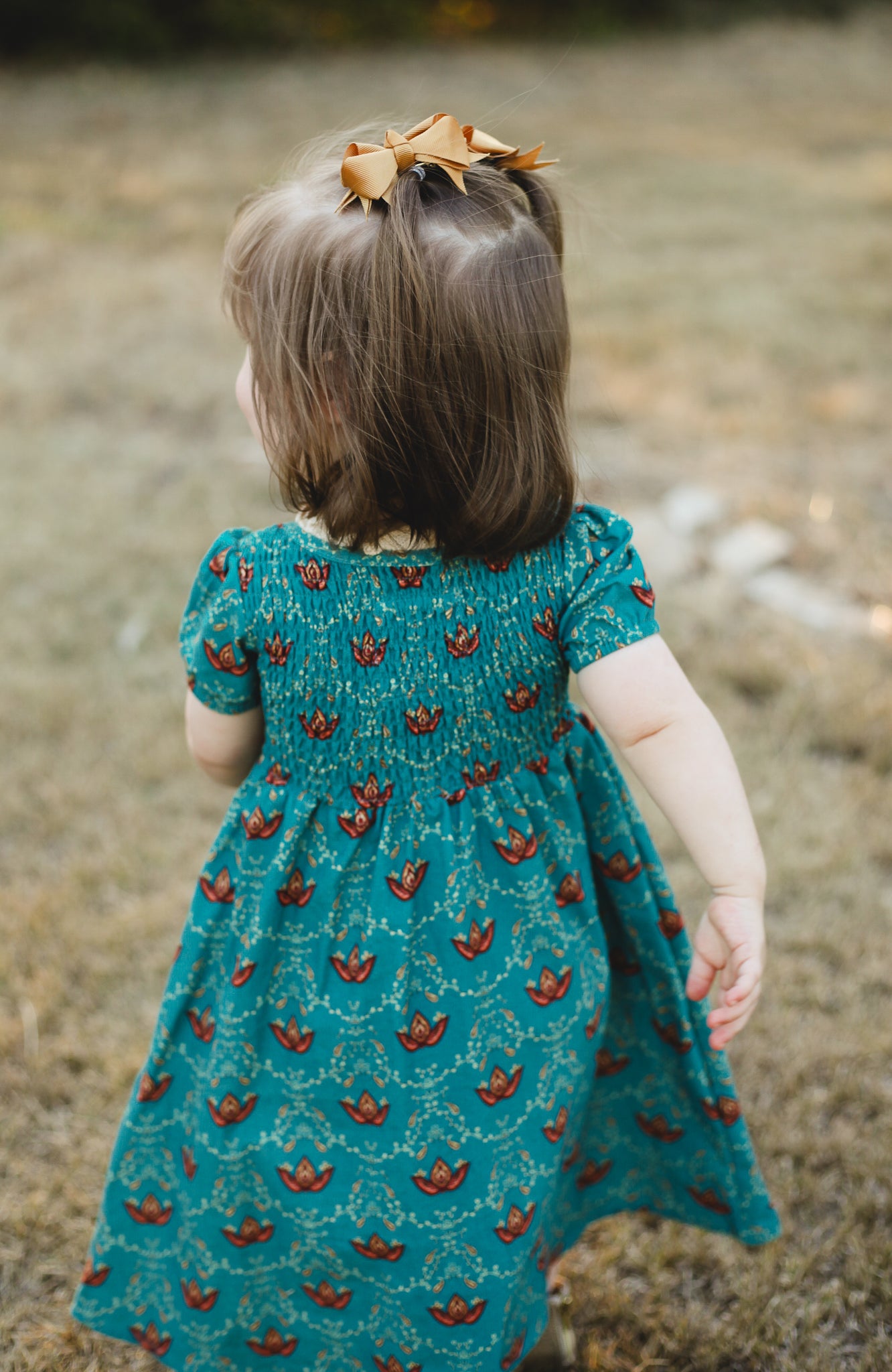 Child wearing modest dress in grassy field outdoors.