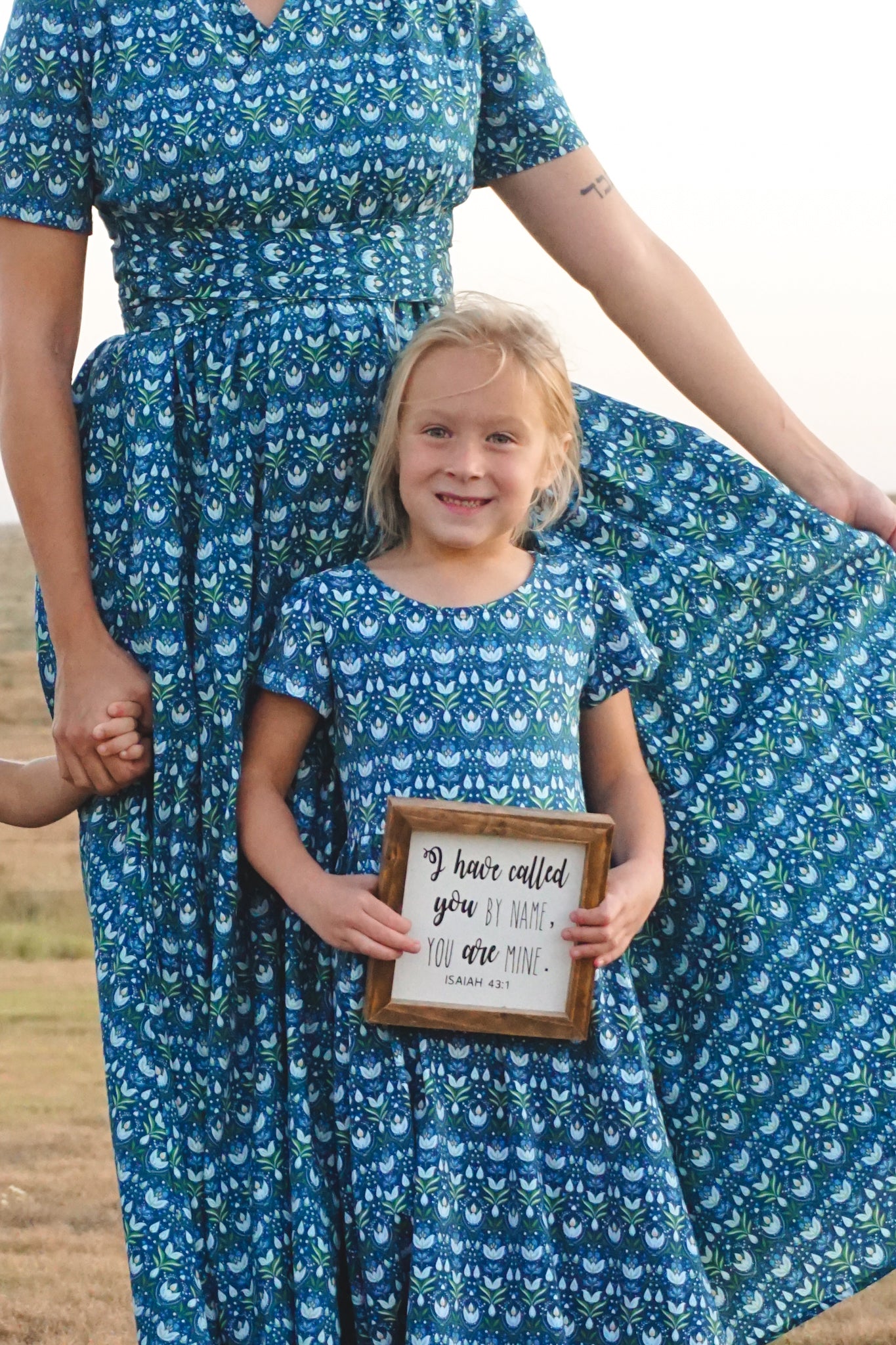 Mother and daughter in matching blue floral dresses holding hands, outdoors
