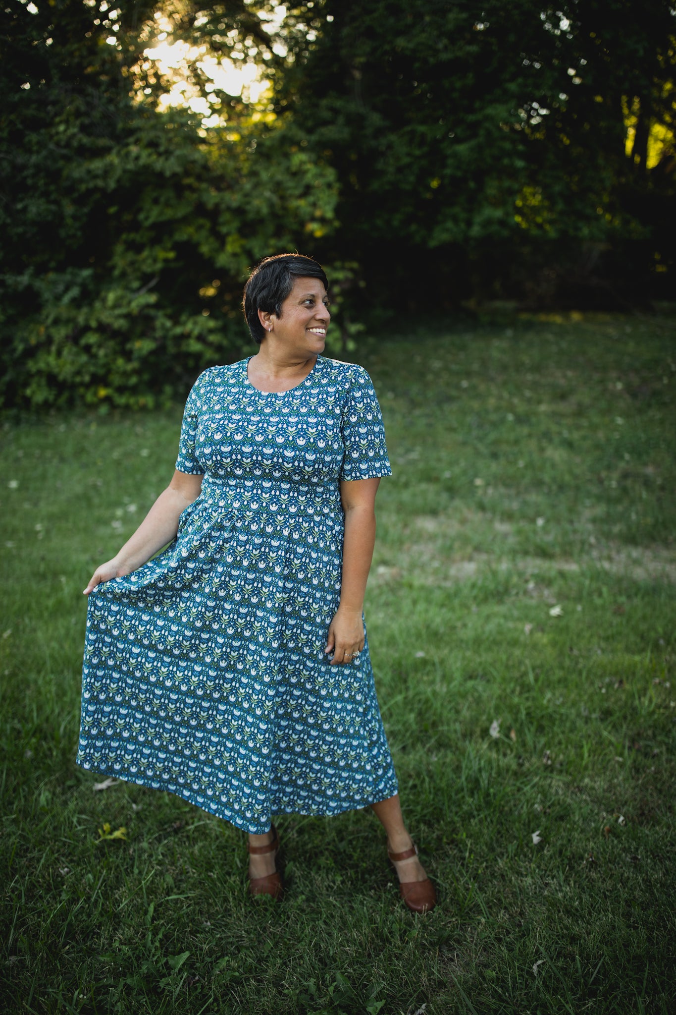 Woman in modest nursing dress, grassy trees background.