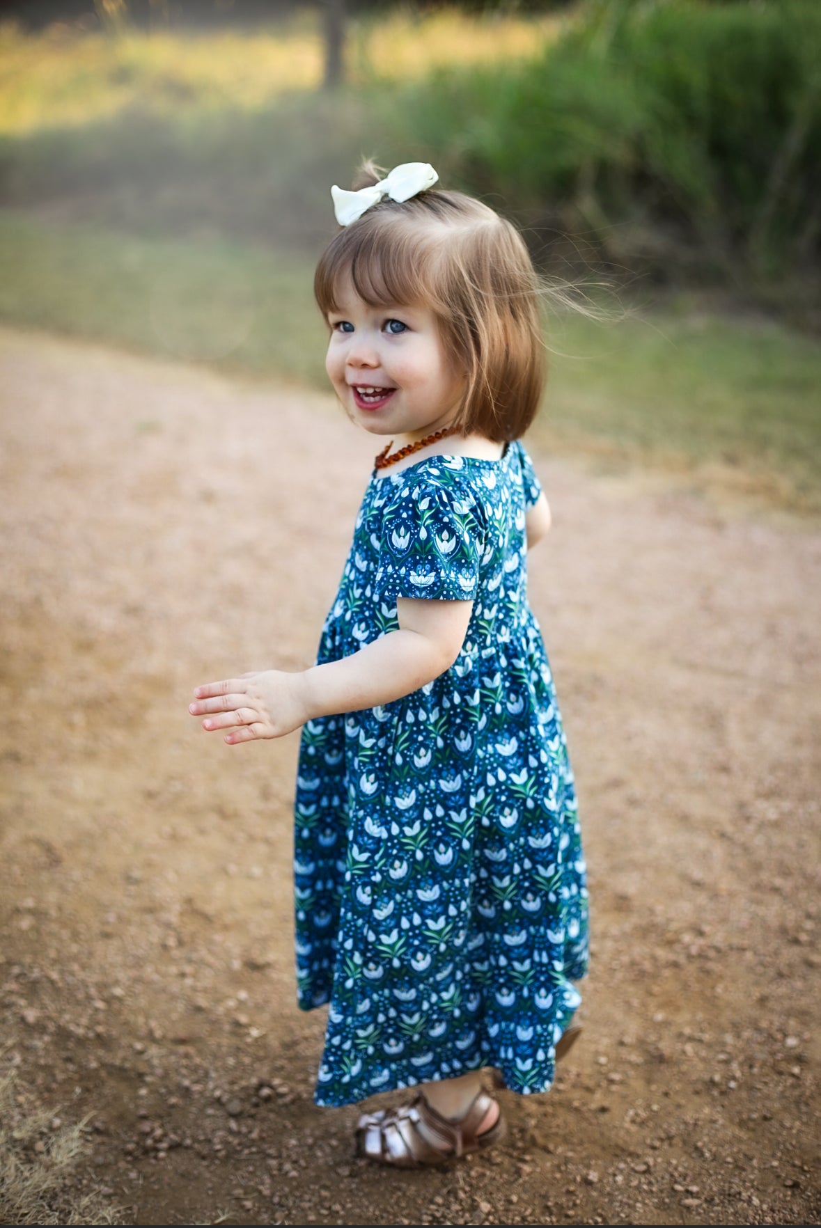 Girl in blue floral dress standing on dirt path