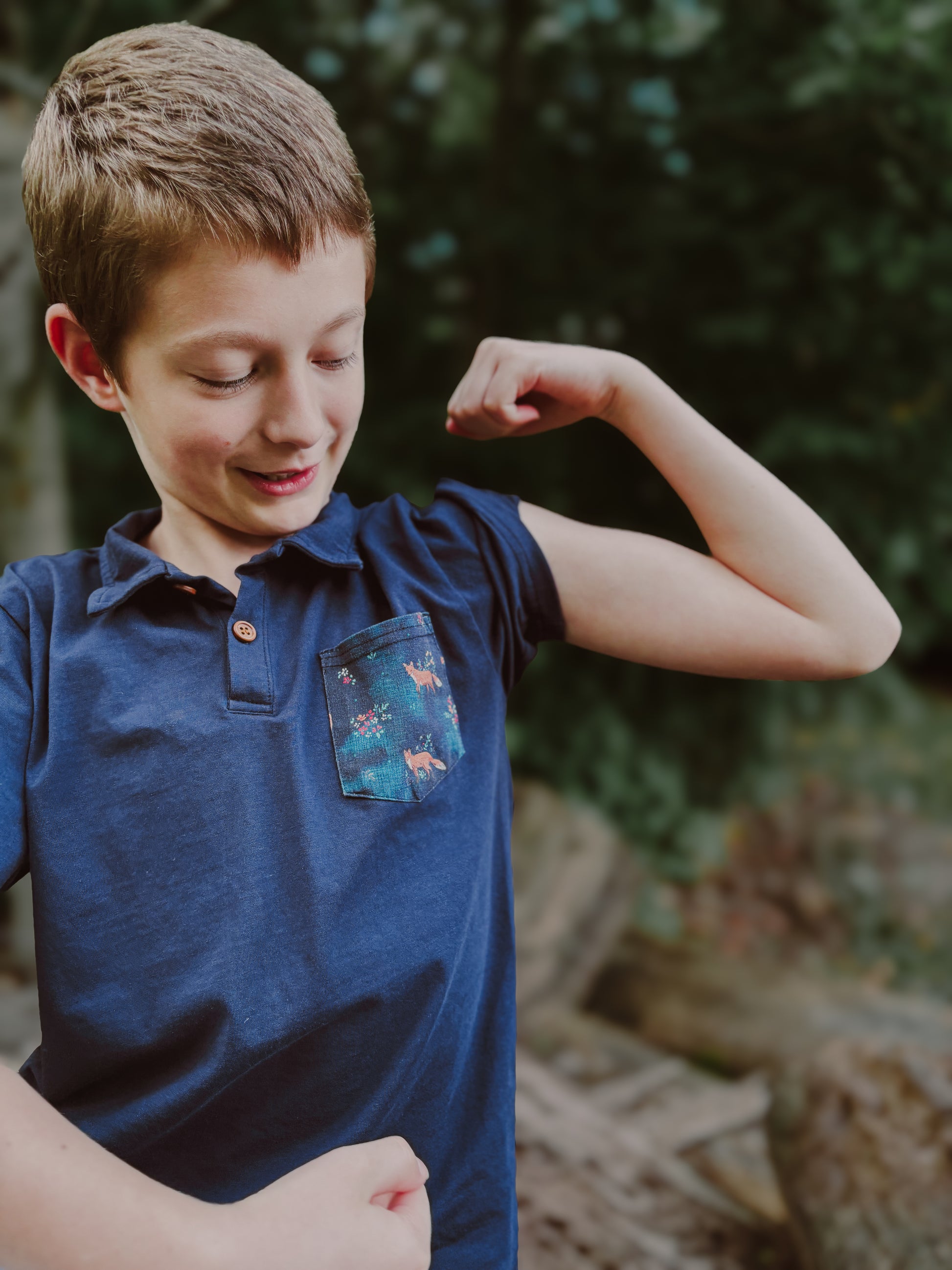 Boy flexing arm outdoors in nature.