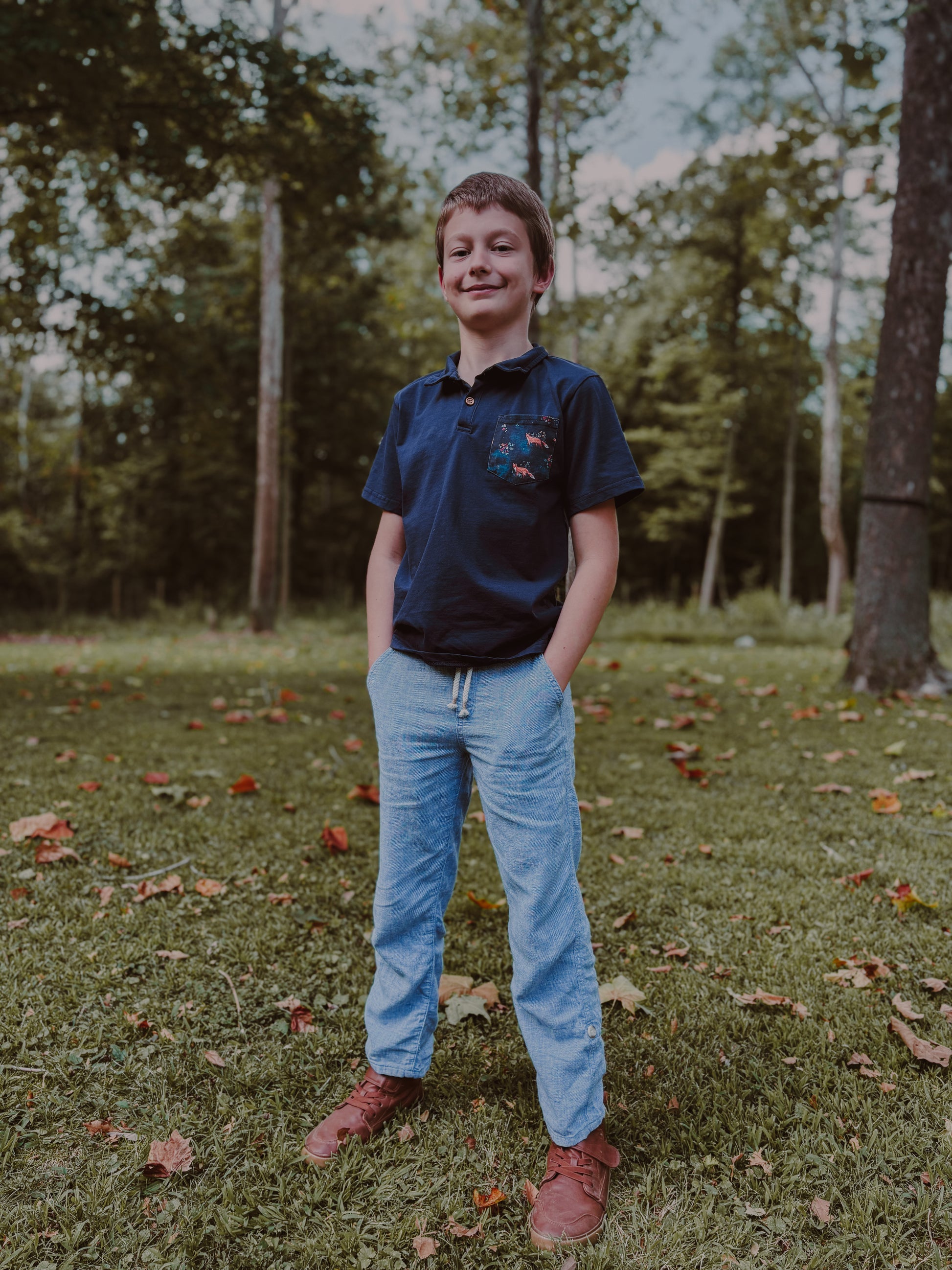 Boy standing in grass with trees.