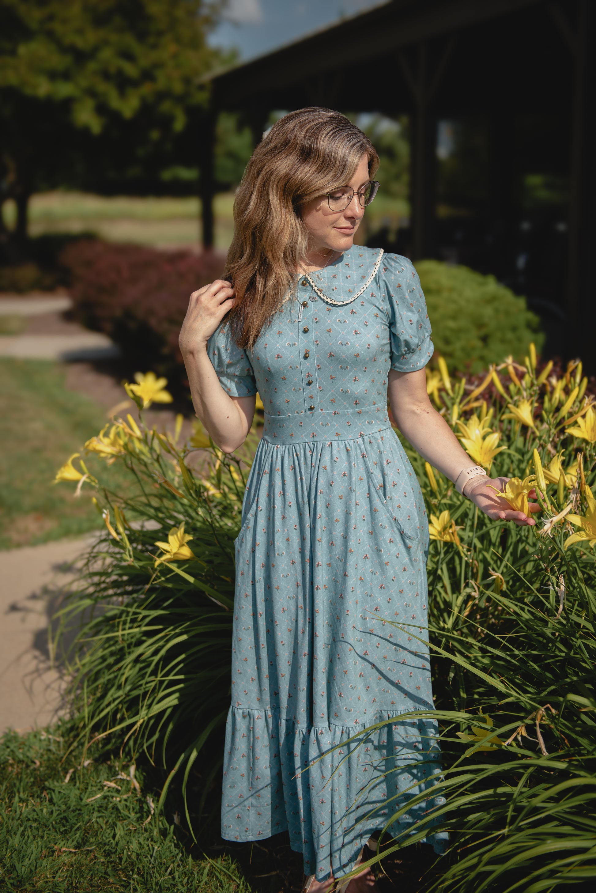 Woman in a light modest nursing dress standing in a garden with yellow flowers