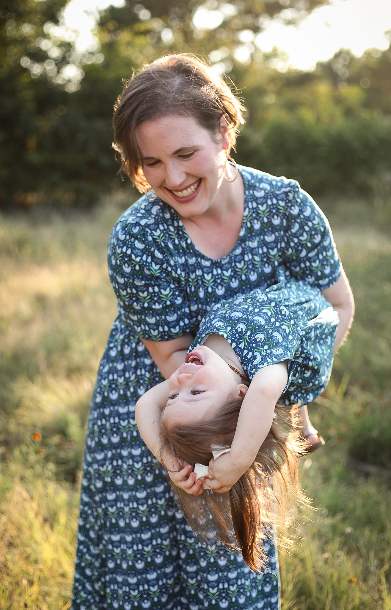Woman in modest nursing dress holding child in field, blue floral pattern.